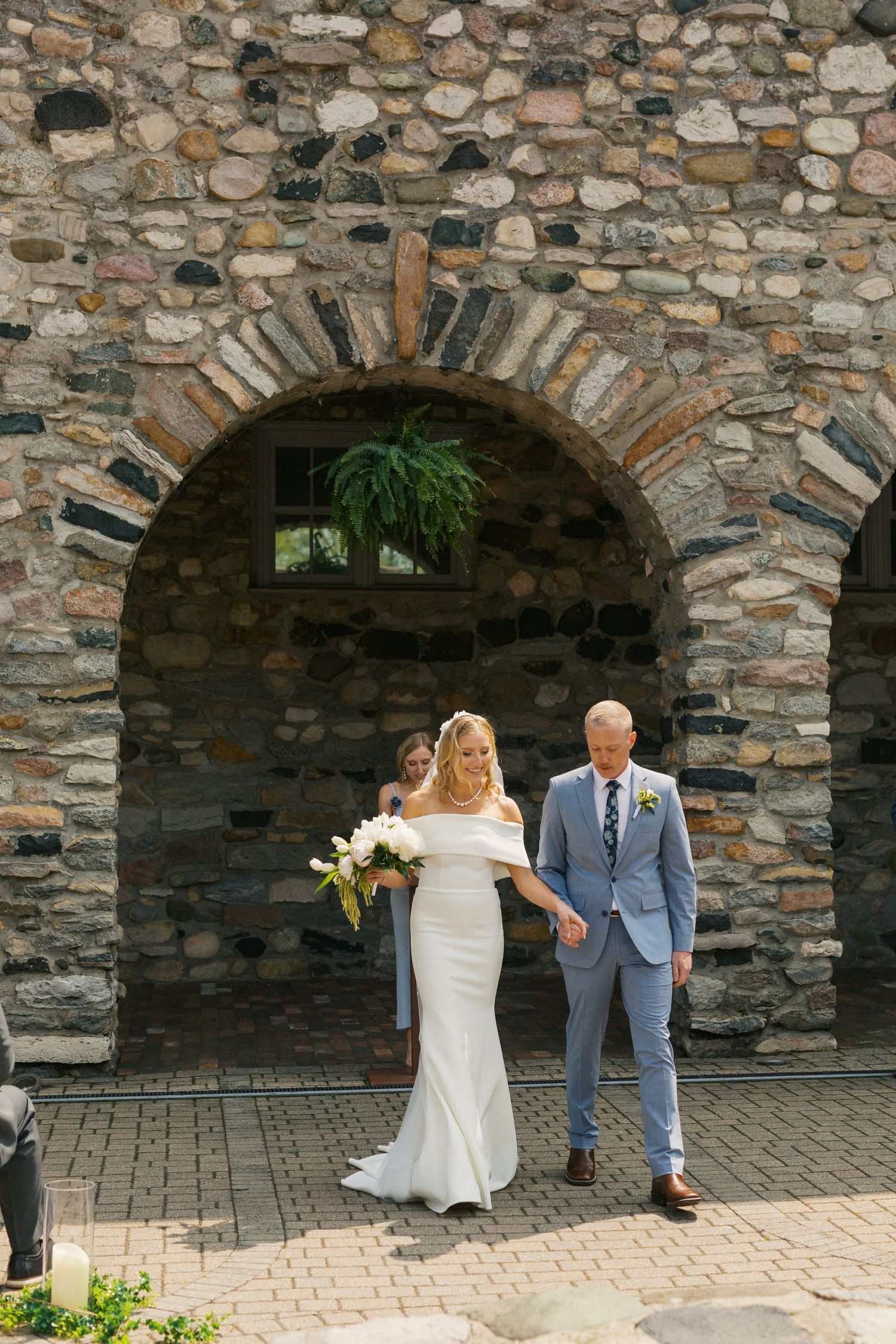 A couple poses under a rustic stone archway during their wedding ceremony.