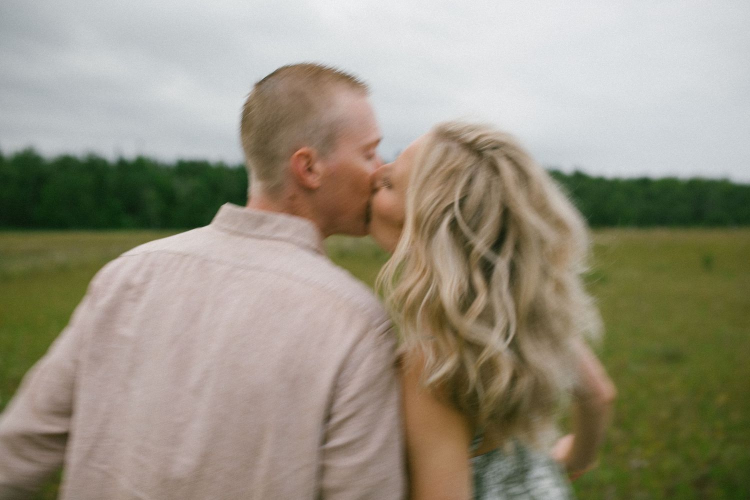 A romantic couple shares an intimate moment in a green field with soft focus and dreamy lighting.