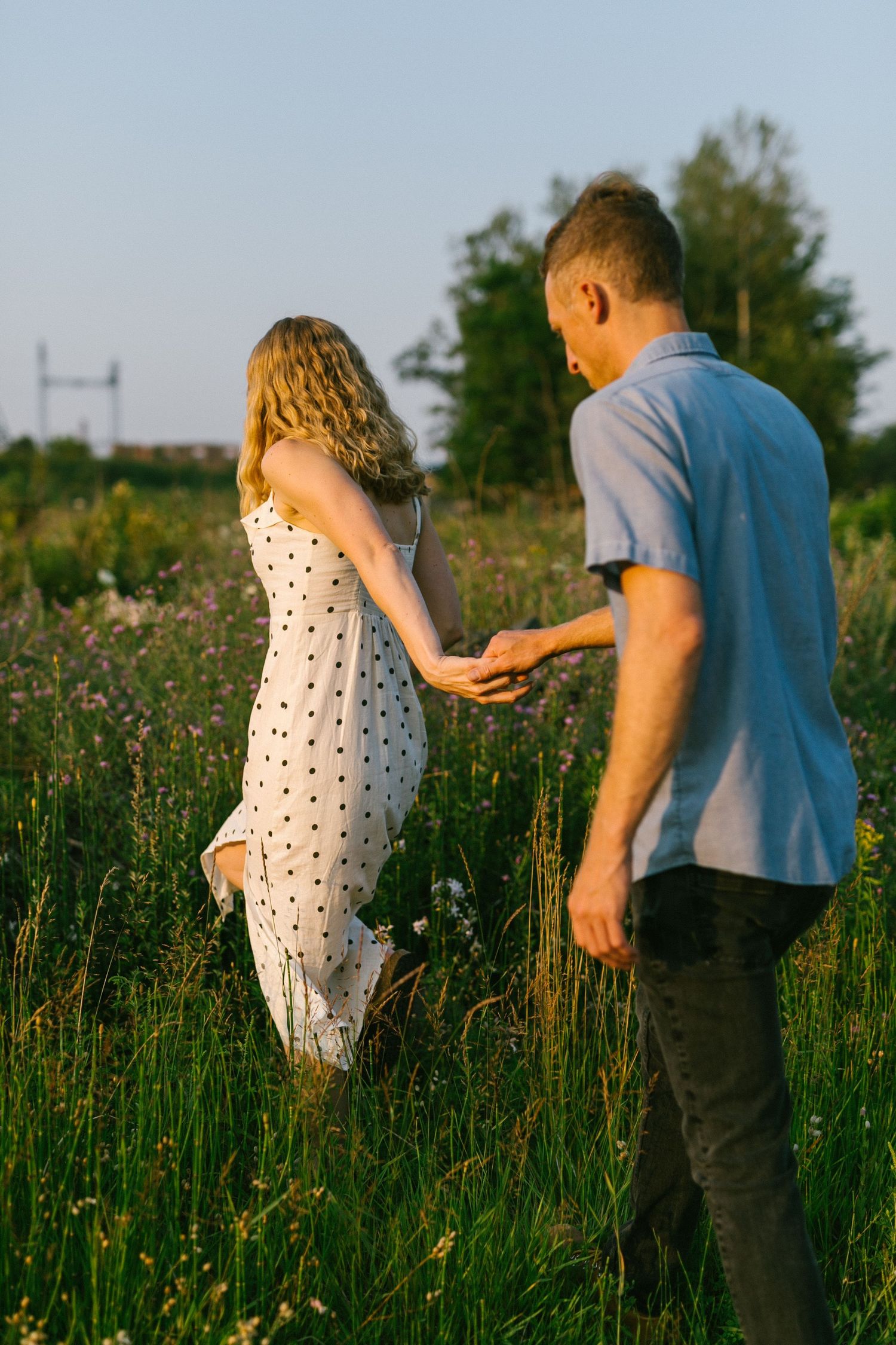Couple walking through tall grass in a field during golden hour.