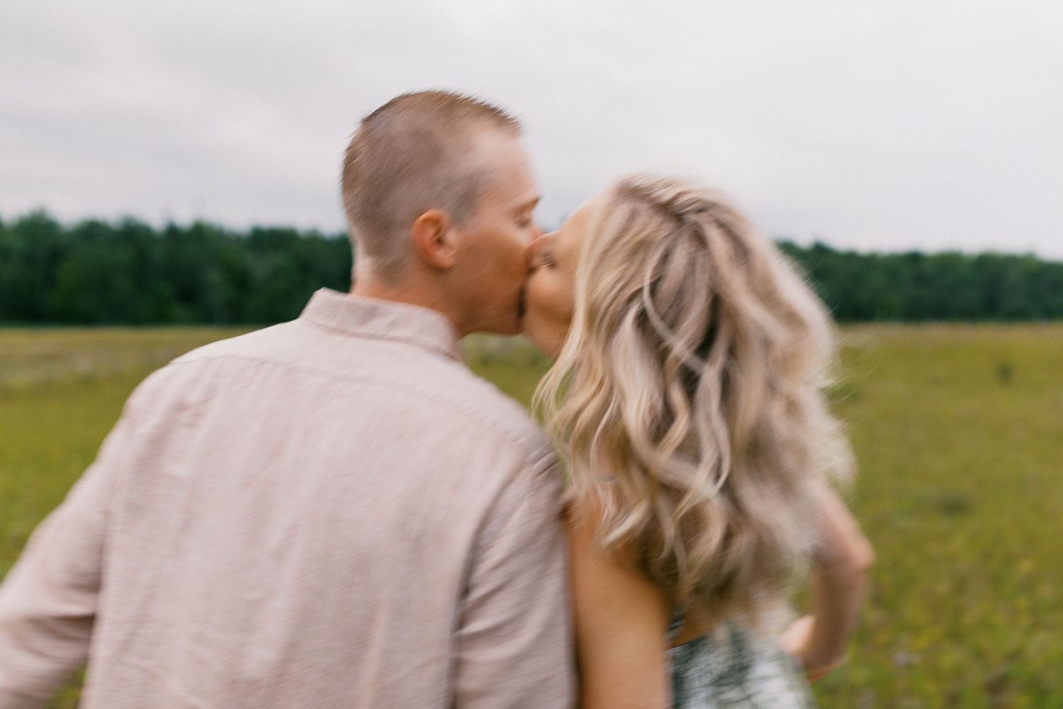 Couple sharing a romantic kiss in a blurred green meadow with forest in the background.