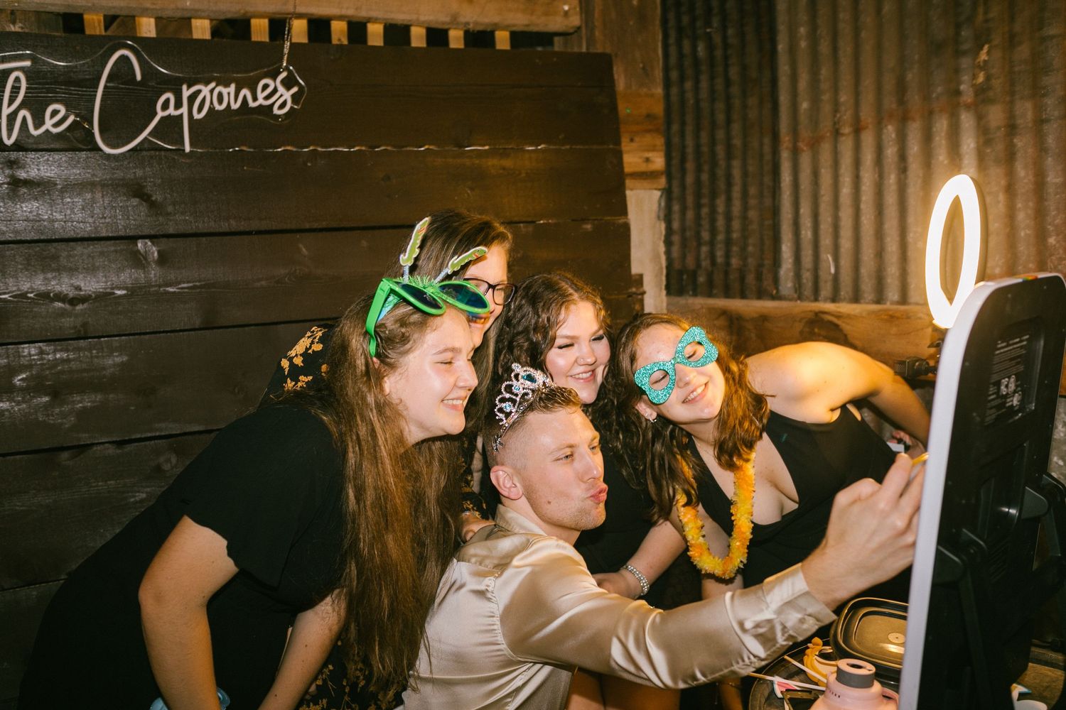 People wearing funny accessories gather around a screen for a festive selfie in dim lighting.