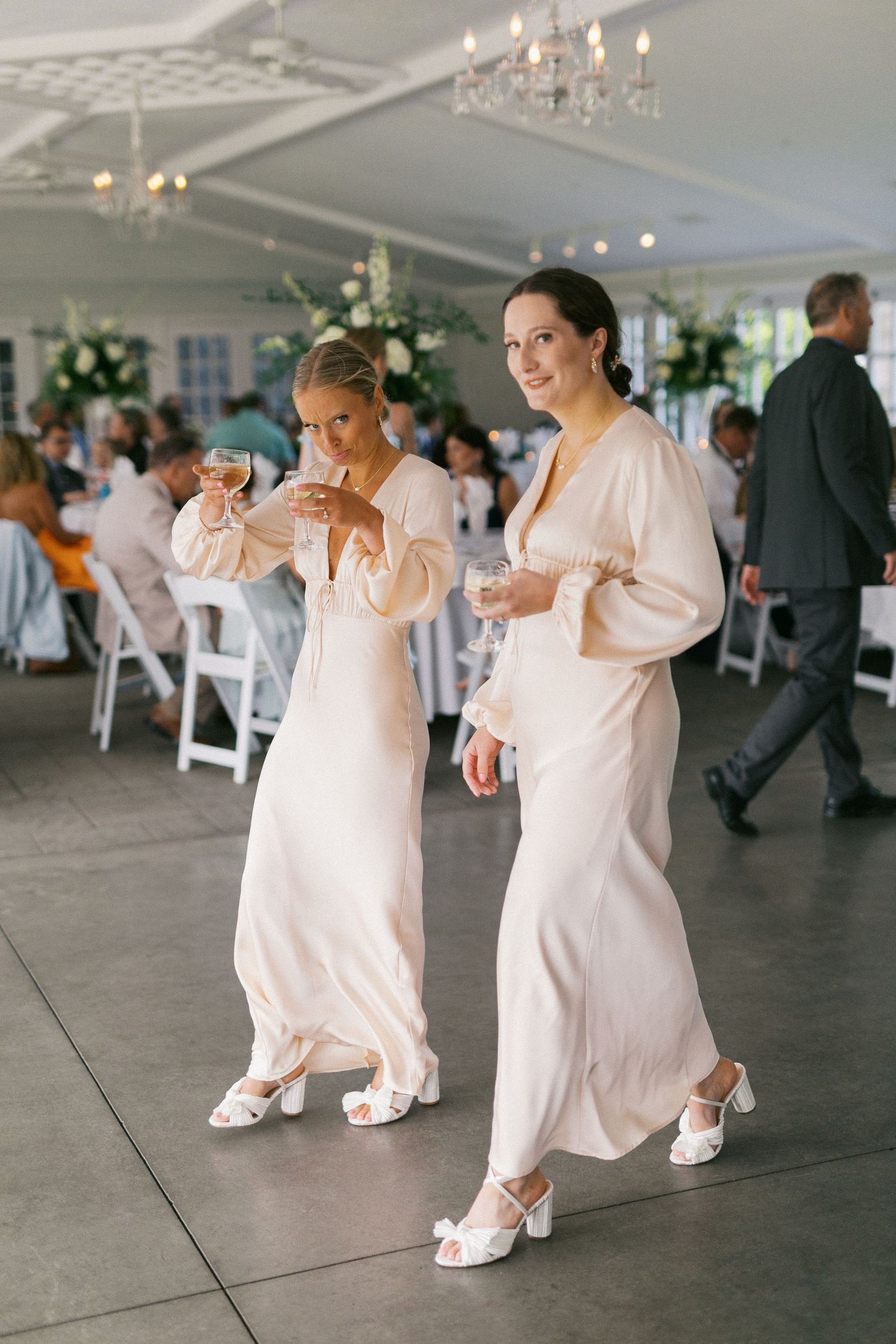 Wedding attendants in flowing white dresses dancing together at a tented reception.