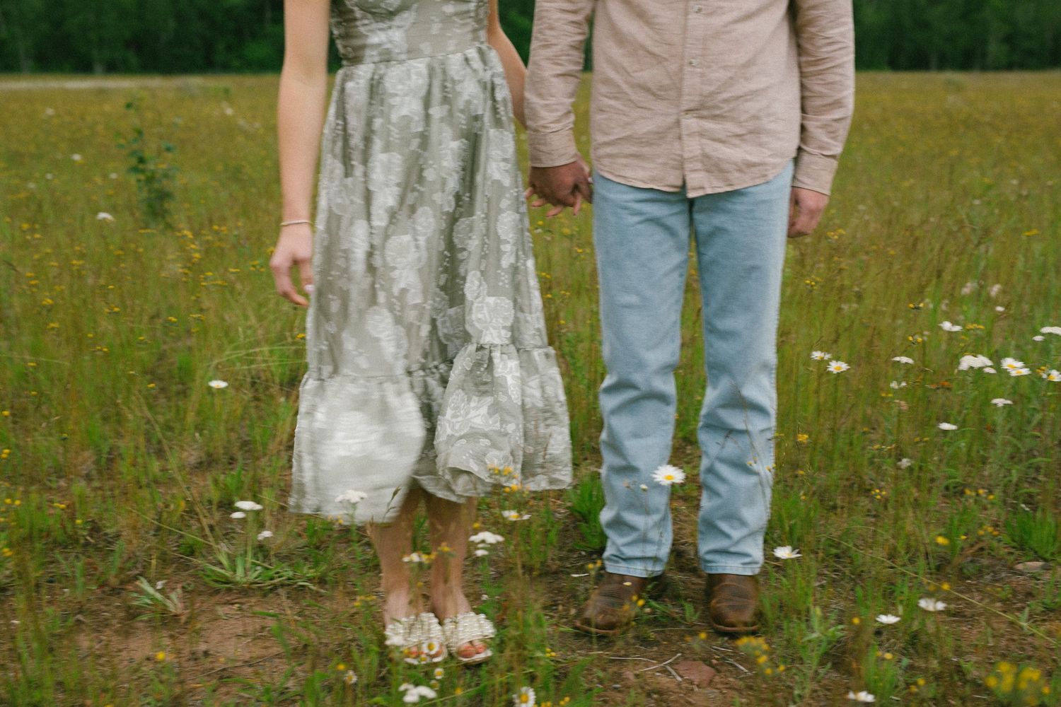 A couple's legs and feet standing together in a grassy field with wildflowers.