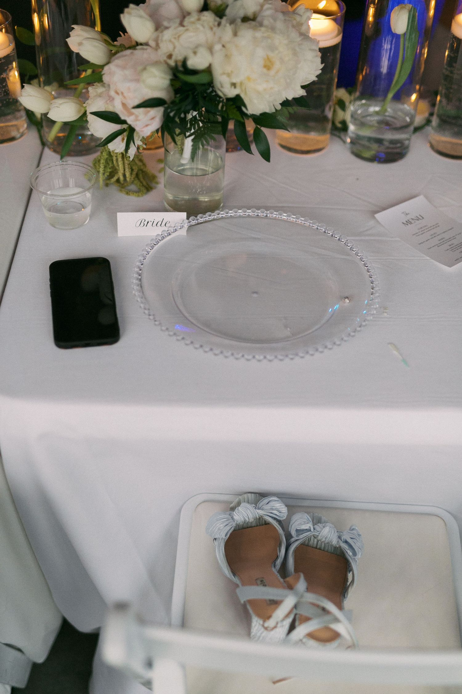 Elegant wedding reception table settings with white floral centerpieces and crystal glassware on crisp white tablecloths.