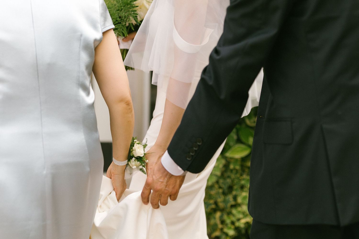 Bride and groom holding hands with a family member during an outdoor wedding ceremony moment.