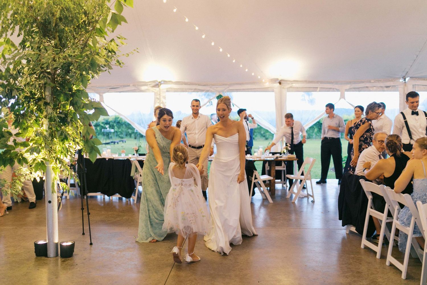 Wedding guests dancing in a white tent reception venue with string lights overhead during a celebration at a vineyard in Michigan.