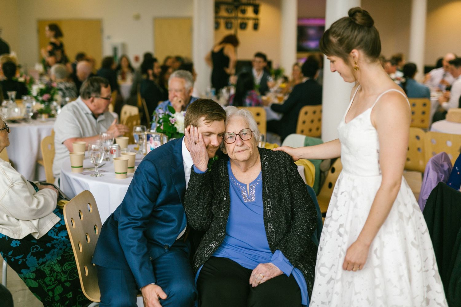Wedding reception scene showing interactions between guests in formal attire at decorated tables.