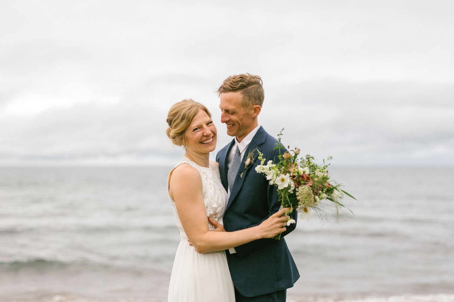 A romantic beach wedding photo with crashing waves and cloudy skies in the background.