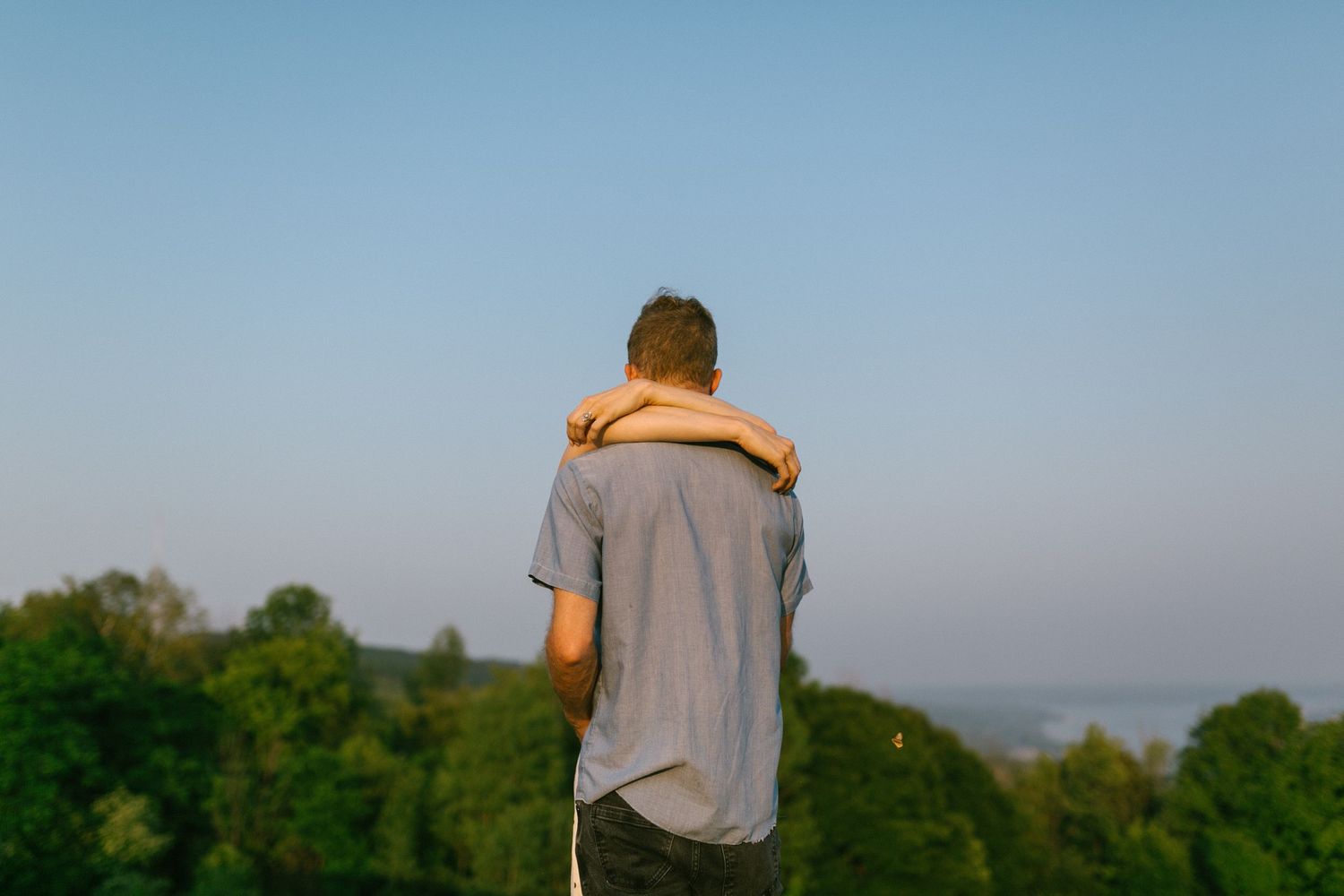 Person in grey shirt looking out over a scenic hilltop vista at sunset.