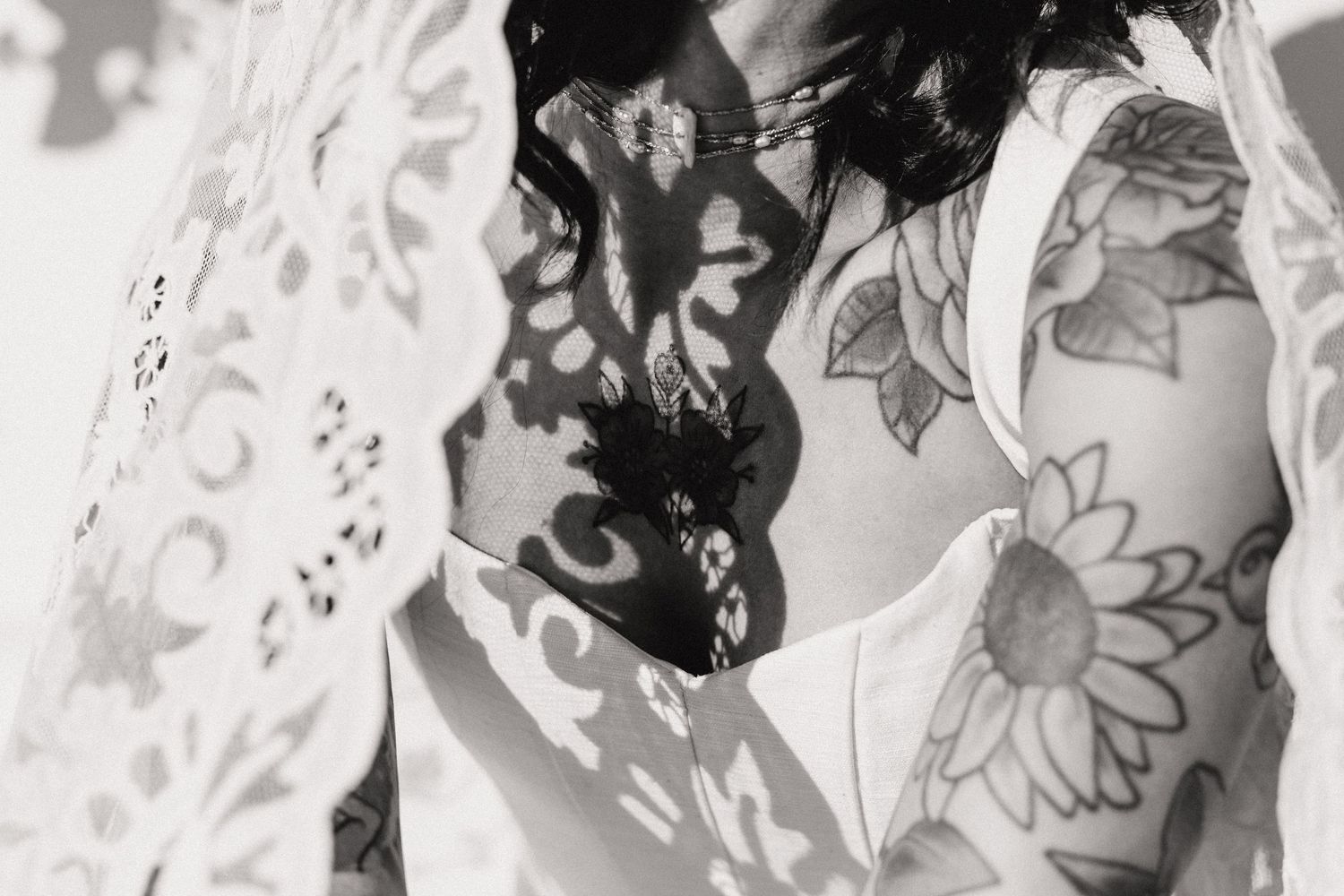 Black and white photo of tattooed arms with floral sunflower tattoos and lace shadow patterns on skin.