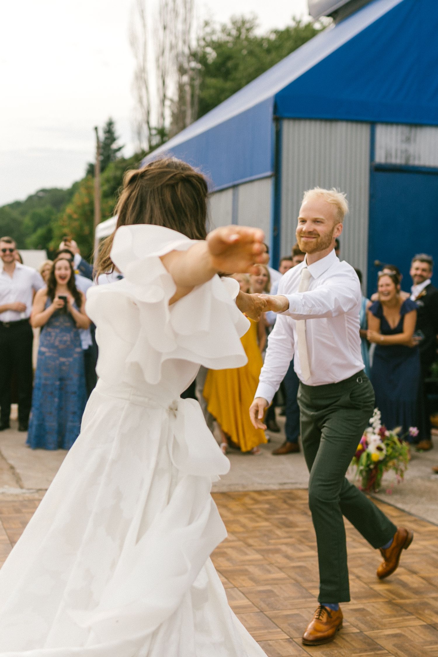 Dancing at a wedding reception outside blue industrial buildings.
