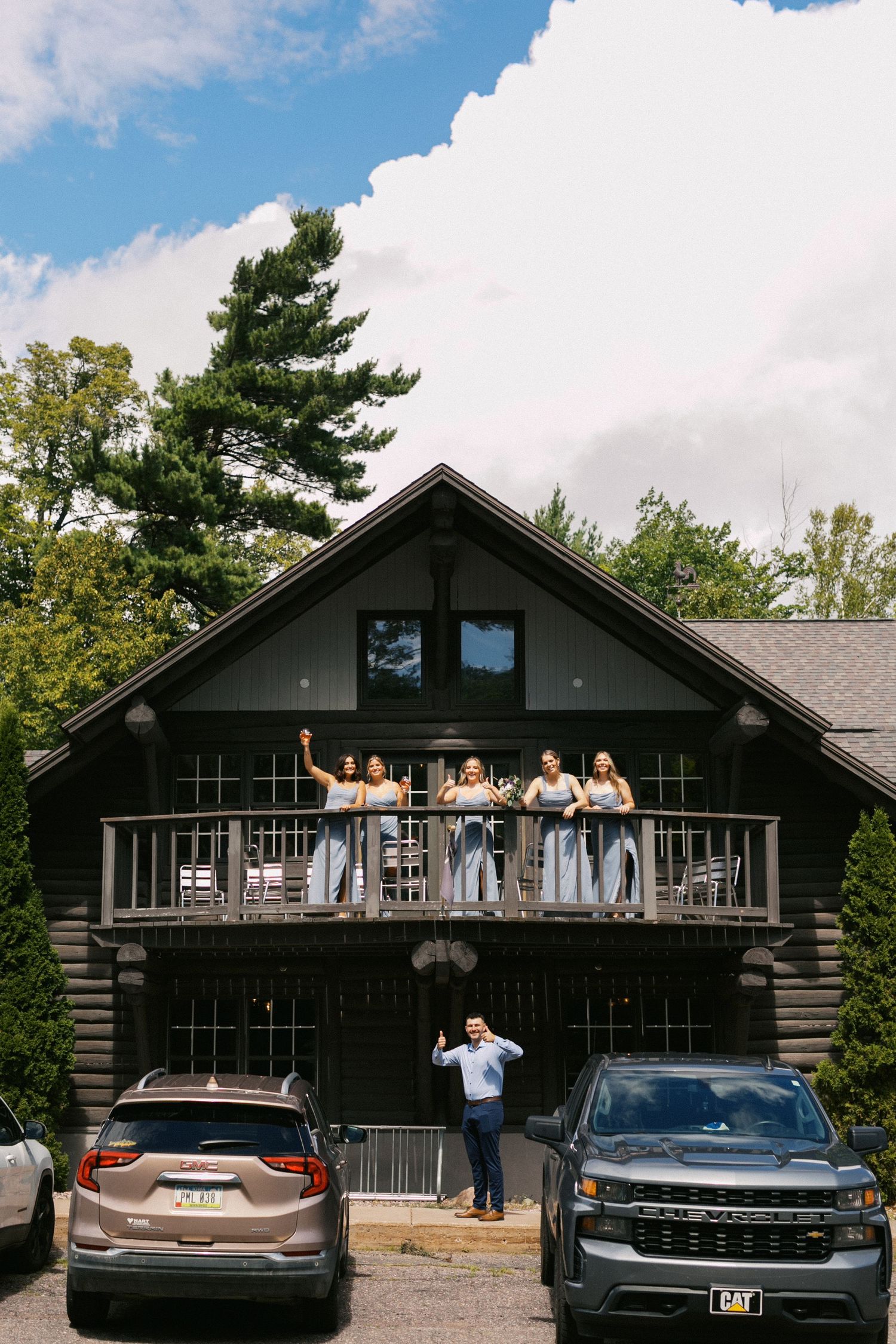 Four sequential photos show people waving from the balcony of a dark wooden cabin with cars parked in front.