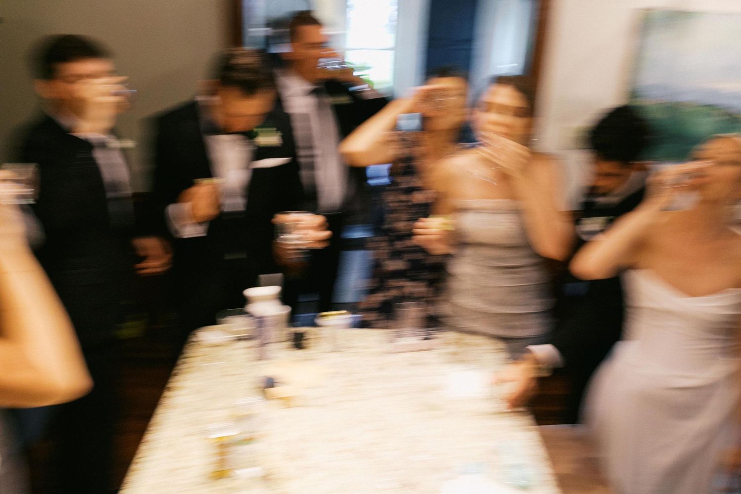 A wedding party drinks a shot in celebration before a wedding ceremony in a blurry action shot.