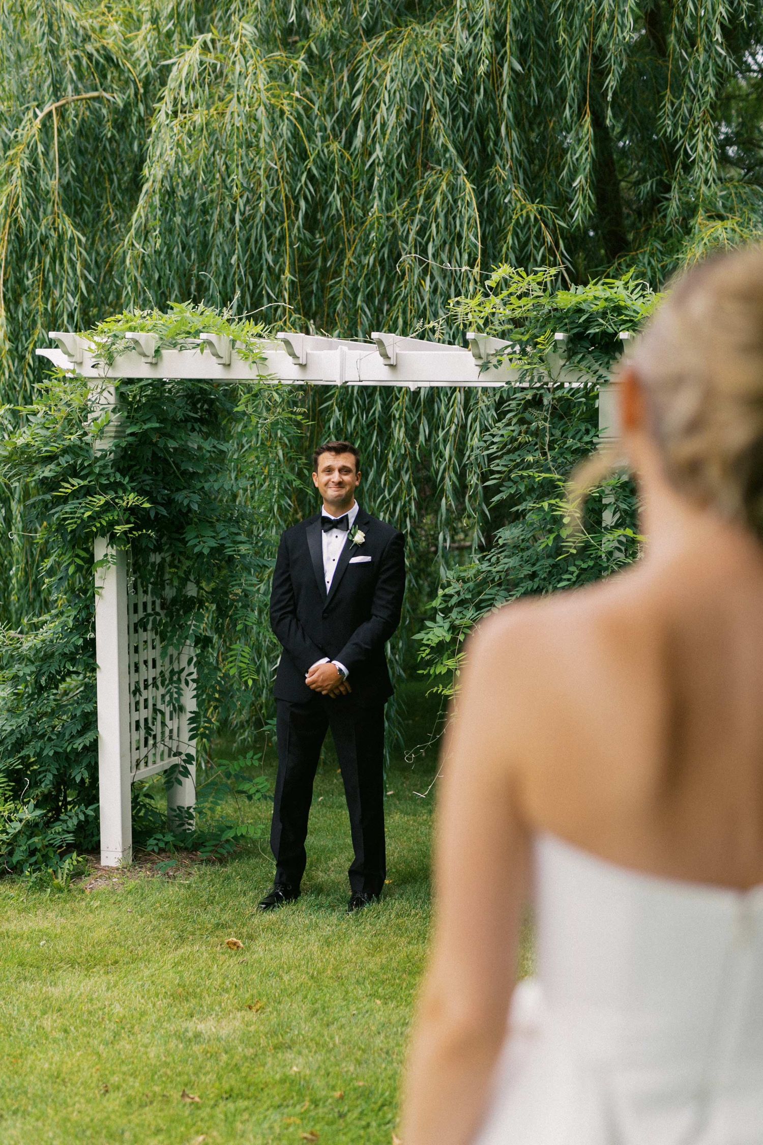 An emotional first look wedding moment captured in a garden setting with lush greenery and white pillars.