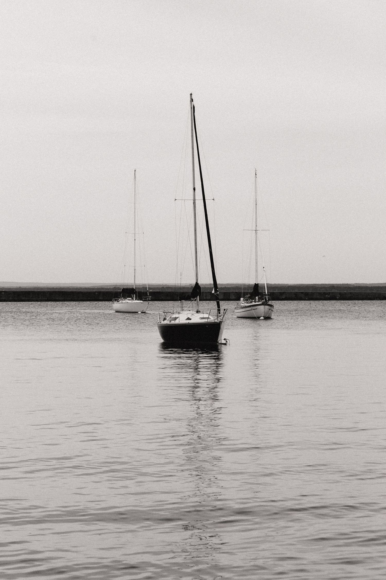Sailboats anchored in calm waters at dusk create a serene black and white seascape.