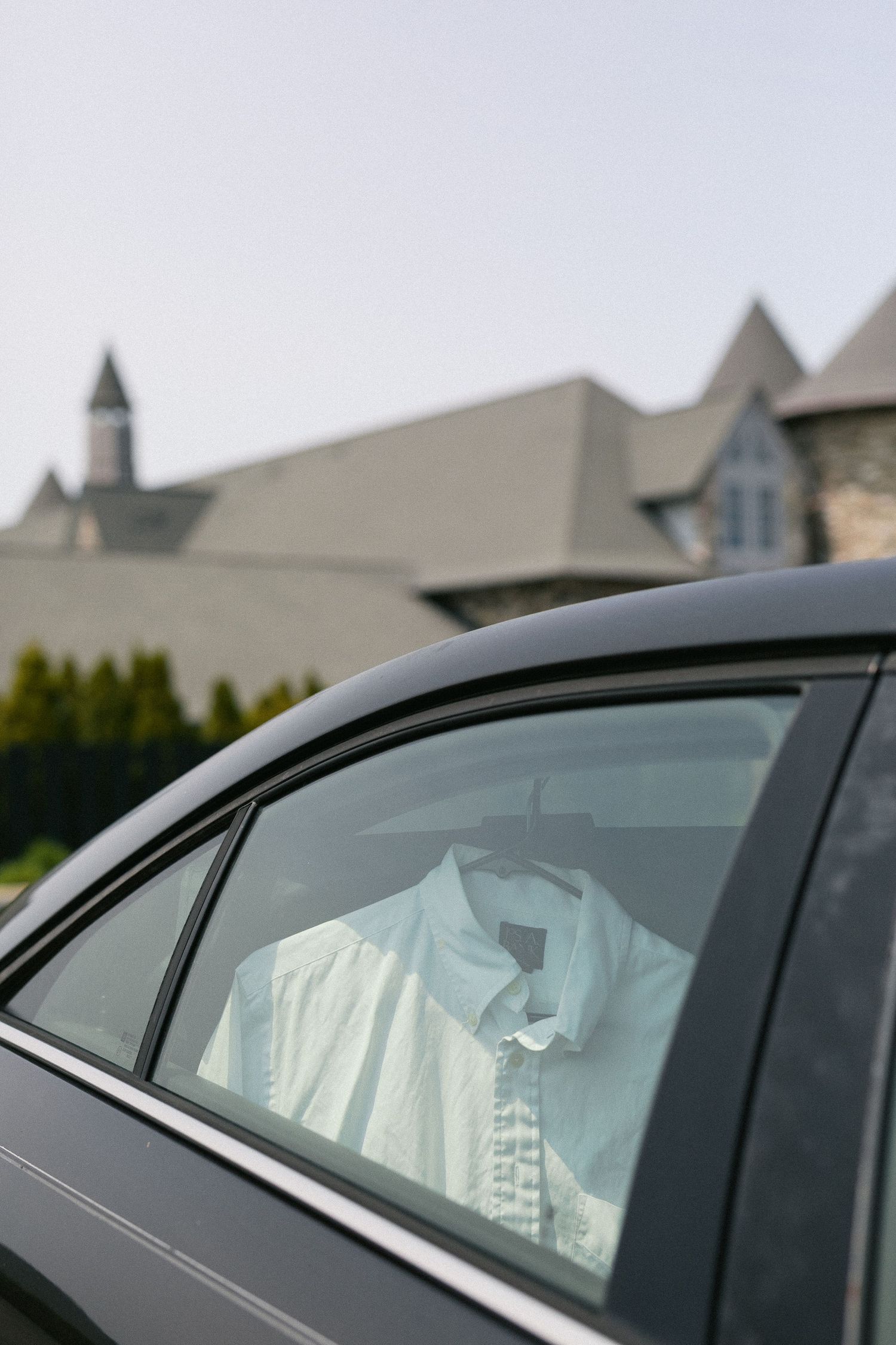 Passenger window view of multiple luxury cars parked in a row outside elegant homes.