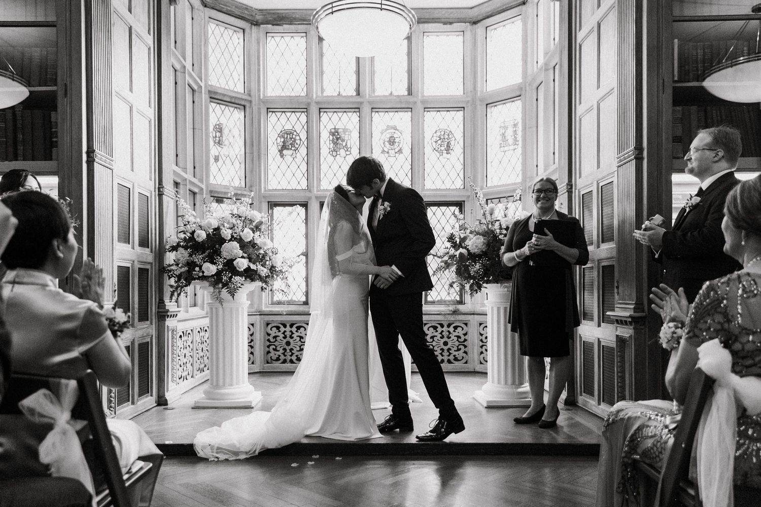 Bride and groom share first kiss at altar with floral arrangements in black and white.