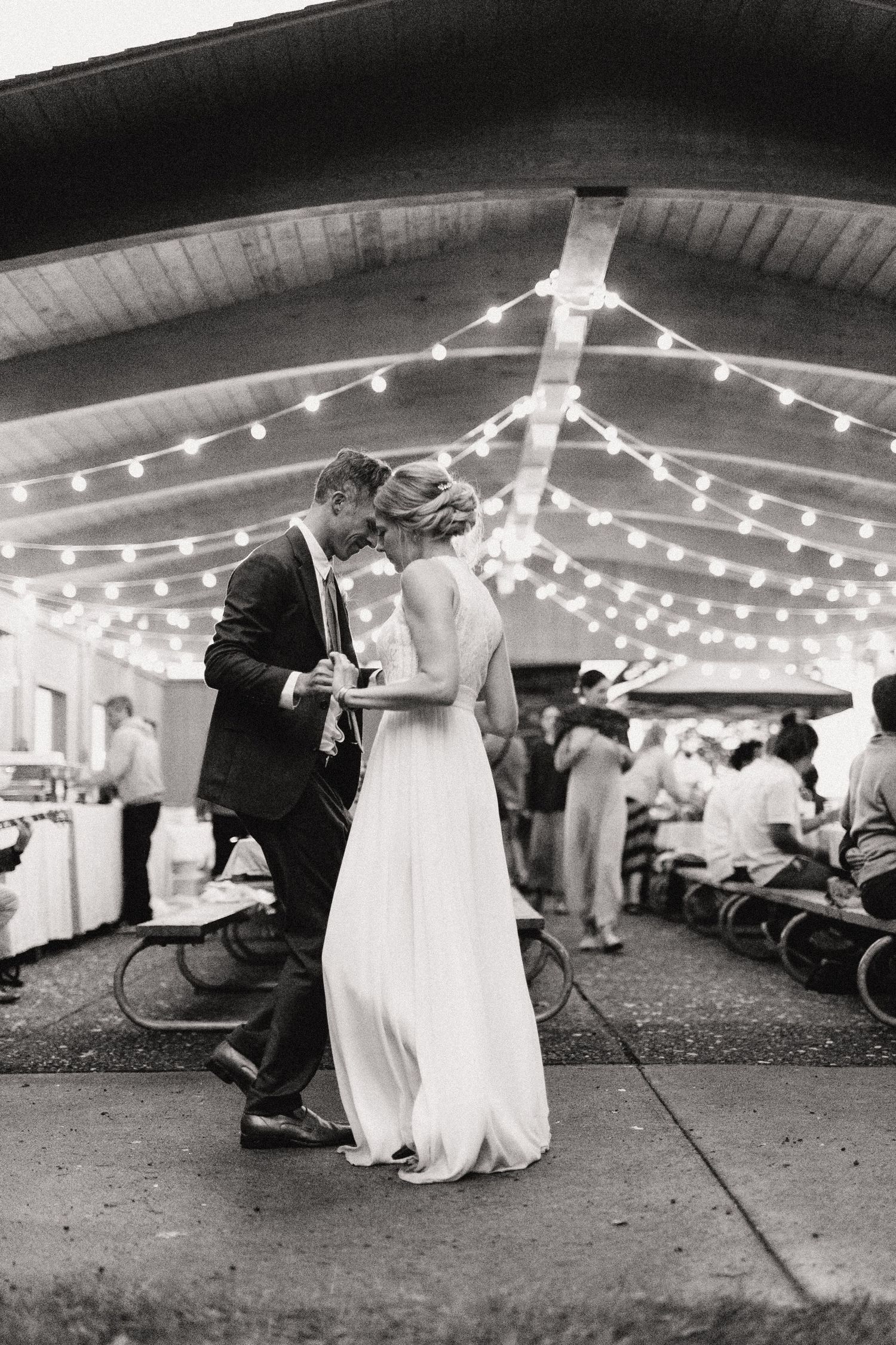 Intimate dance moment under string lights at outdoor wedding reception.