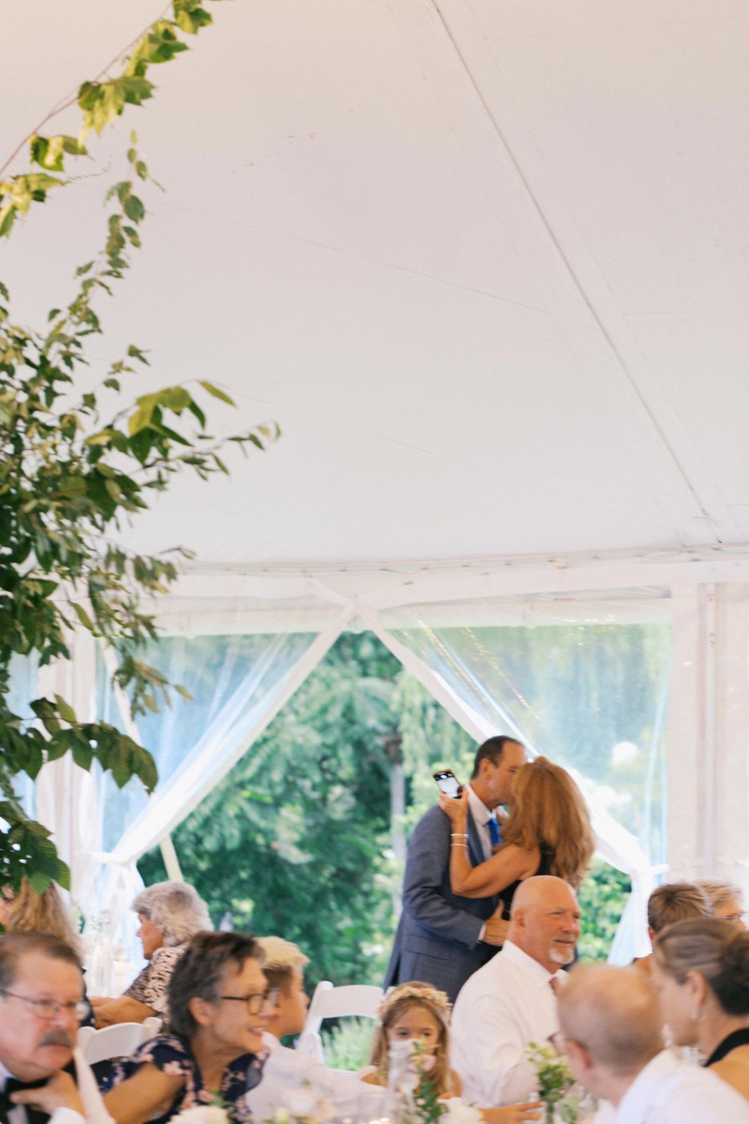 Wedding guests celebrate and dance together under an elegant white tent during an outdoor reception celebration.