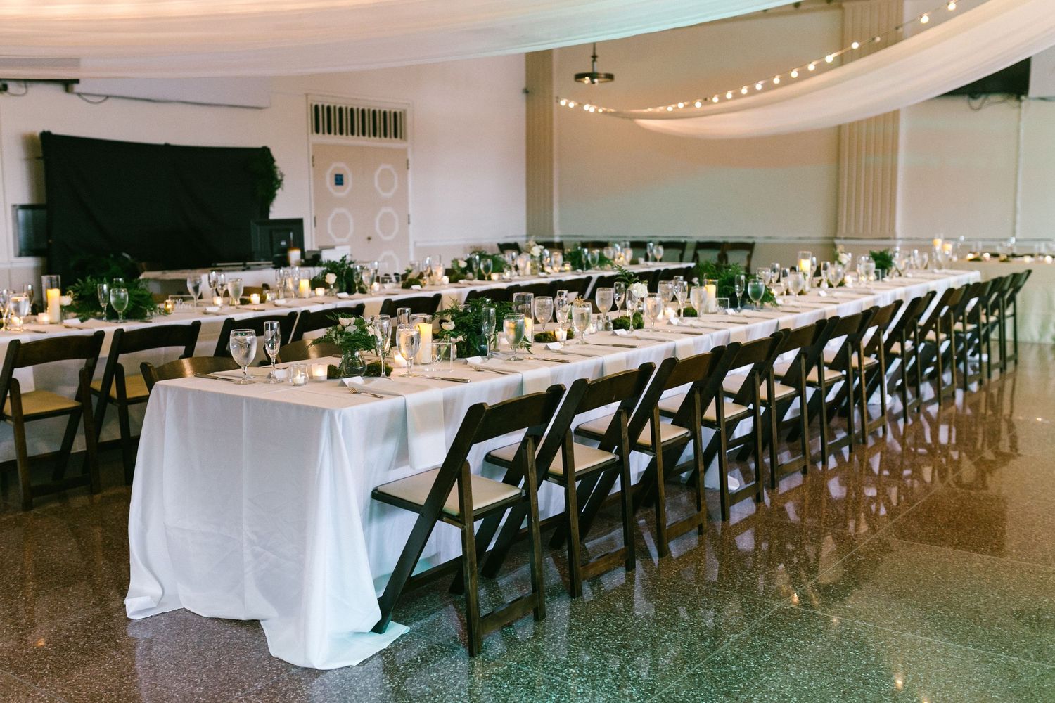 A long banquet hall decorated with white tablecloths and black chairs set up for an elegant wedding reception.