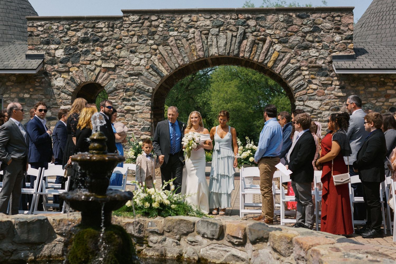 Wedding ceremony setup against a rustic stone wall backdrop with guests seated outdoors.