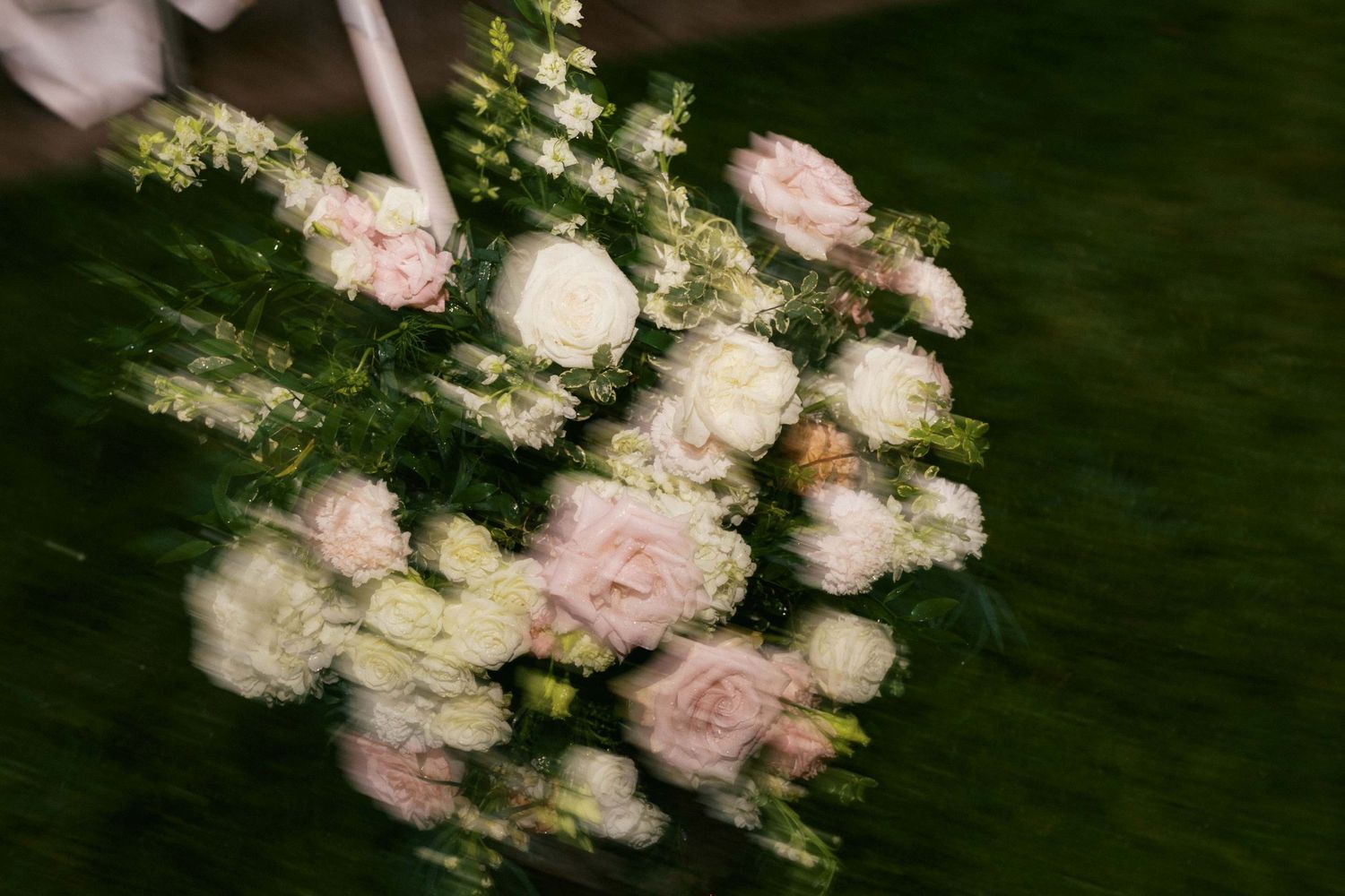 Soft pink roses and white flowers create a dreamy, motion-blurred bouquet against a dark green background.