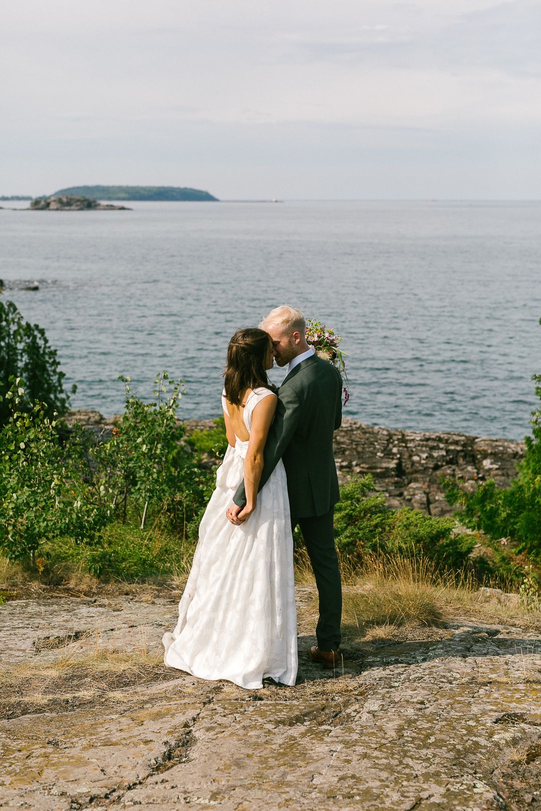 A couple shares a romantic moment on a rocky coastal cliff overlooking the ocean on their wedding day.