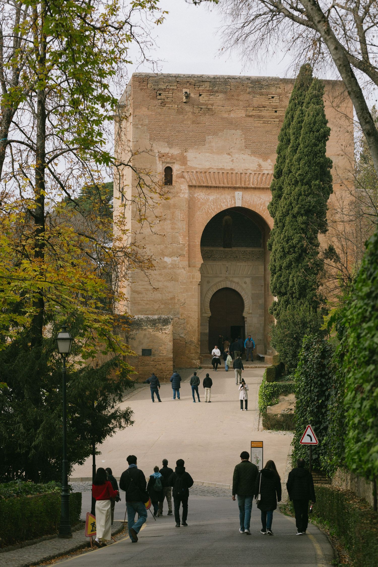 Visitors walking towards the historic Justice Gate entrance at the Alhambra palace complex in Granada, Spain.