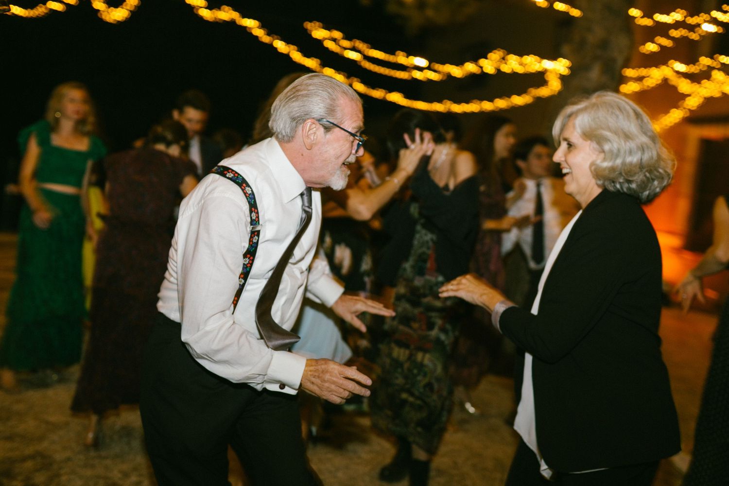 Elderly couple dancing together at a festive evening event with twinkling golden lights in the background.