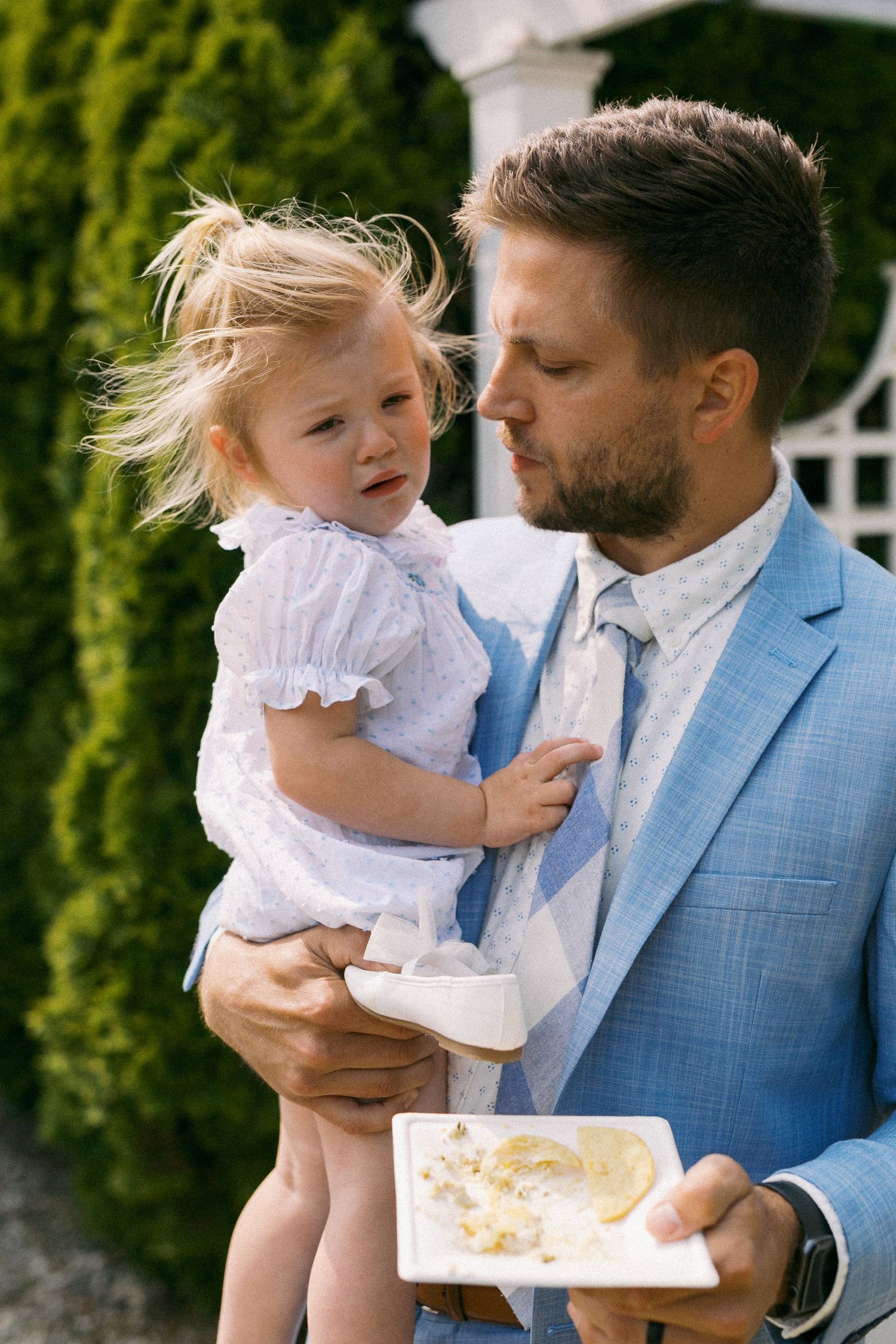 A sweet moment between parent and child under evergreen trees at an outdoor gathering.