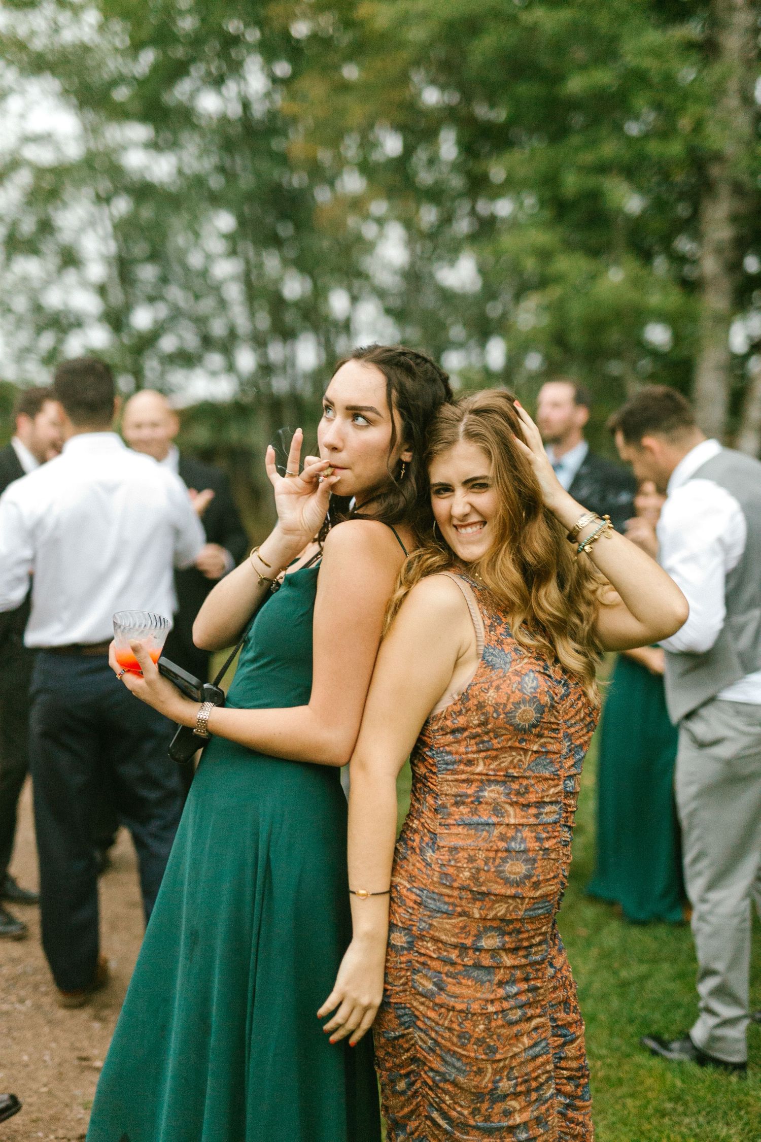 Two guests in formal dresses pose playfully at an outdoor wedding reception.