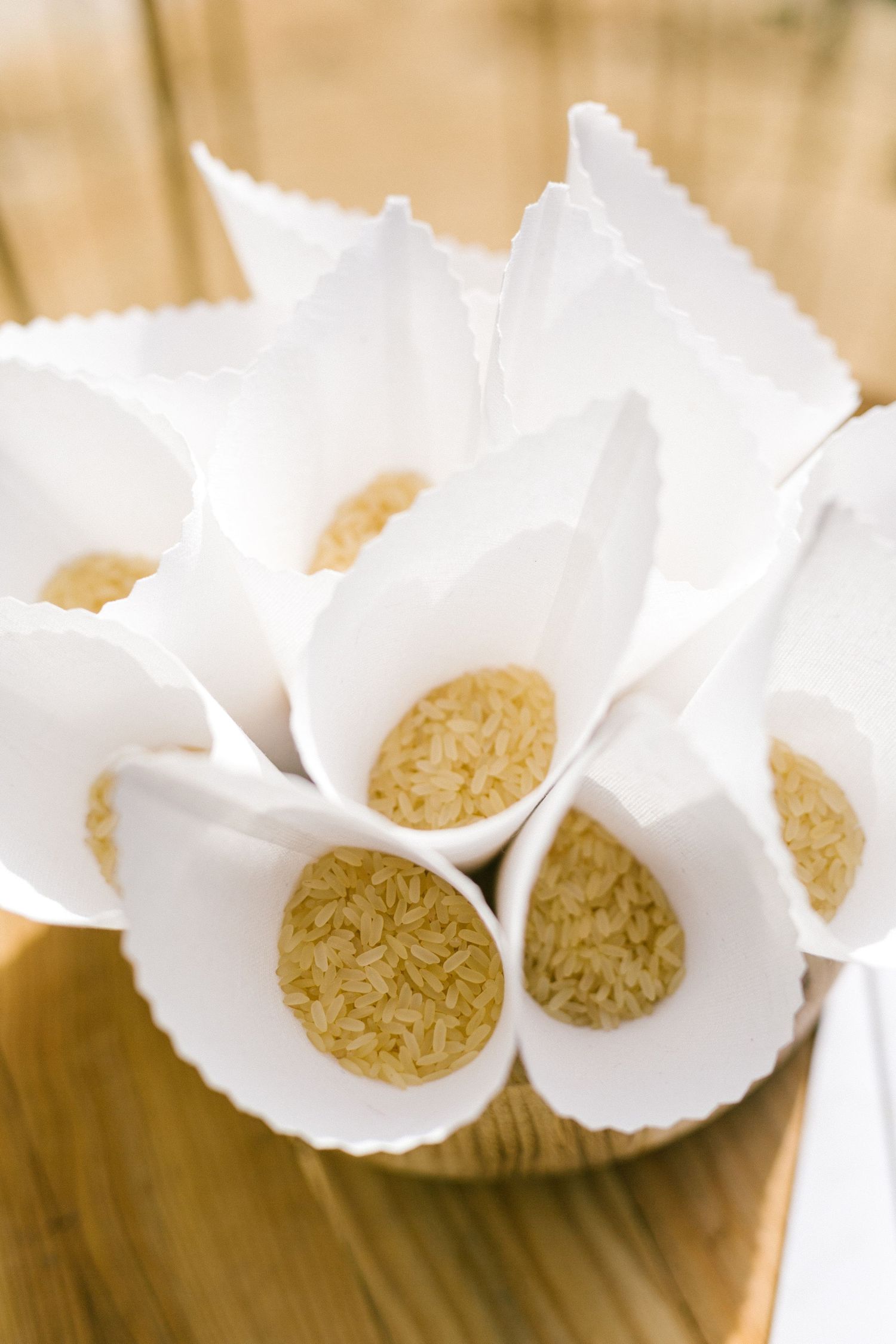 Small paper cones filled with brown rice displayed on wooden surface in an artistic arrangement.