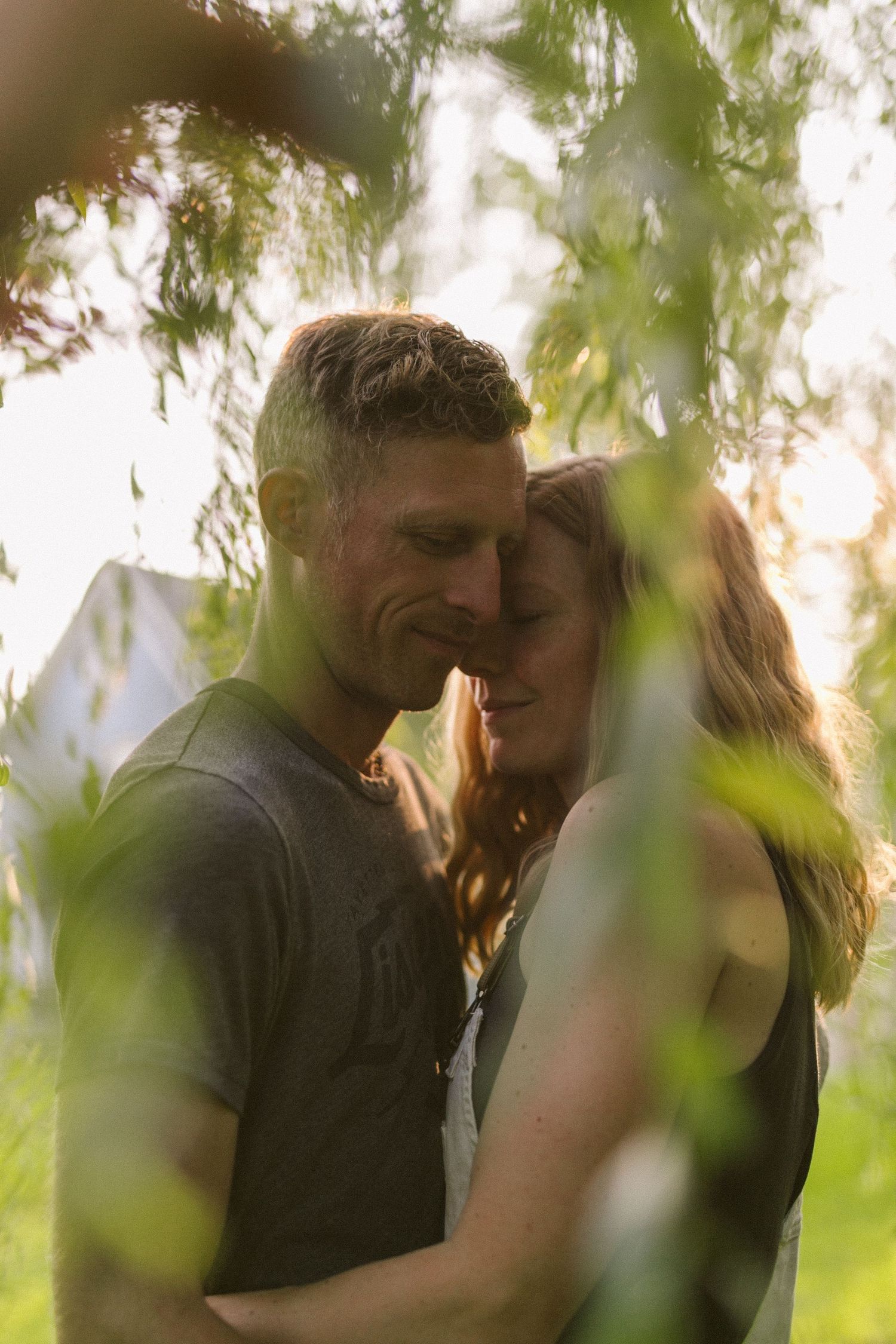 A tender moment captured between two people among green foliage at sunset.