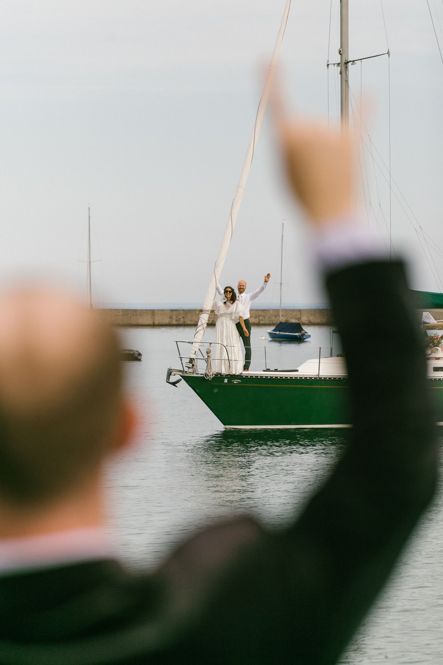 People wave to a sailboat from the shore during a celebration.