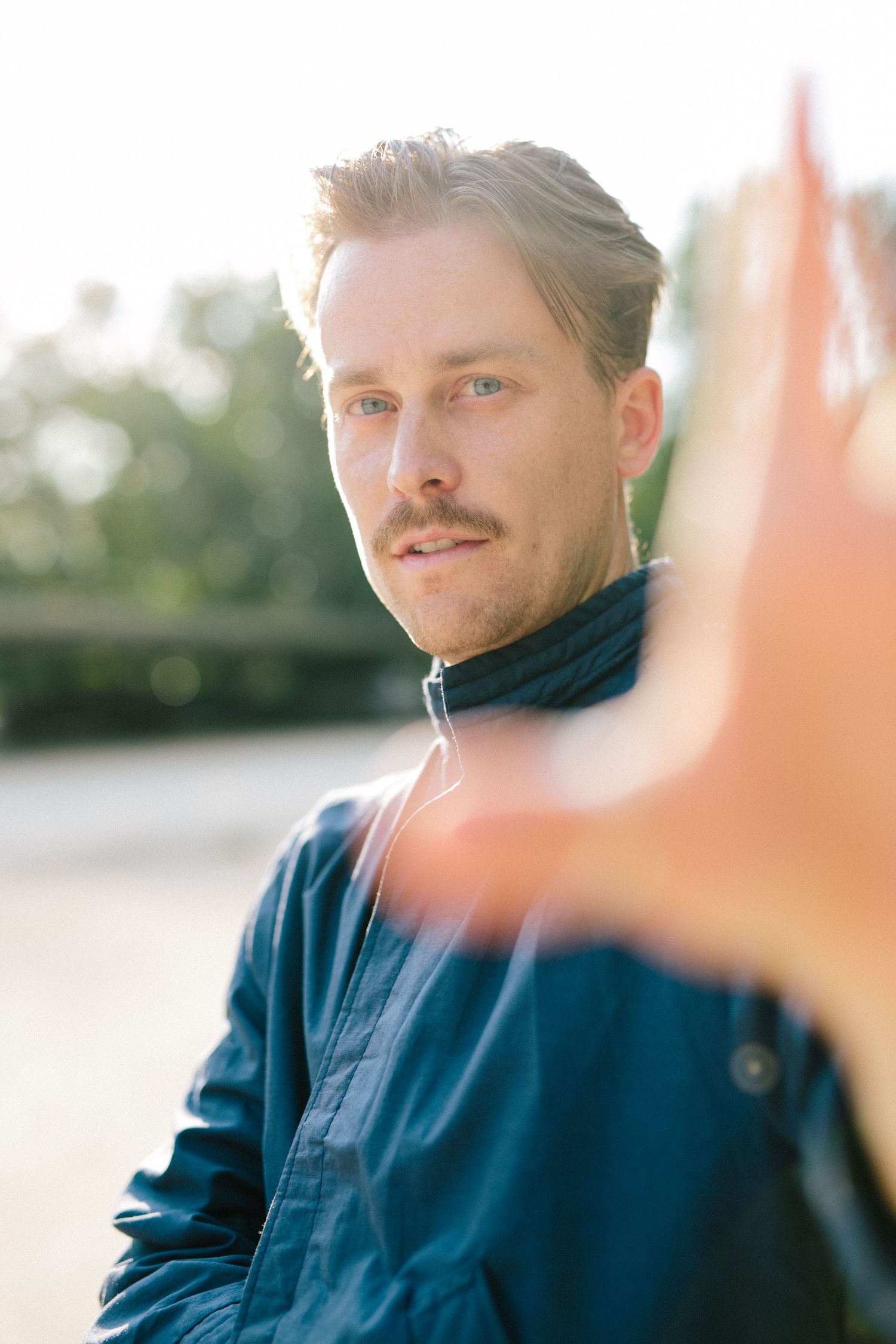 Stylish outdoor portrait featuring a navy jacket and mustache in warm sunlight.