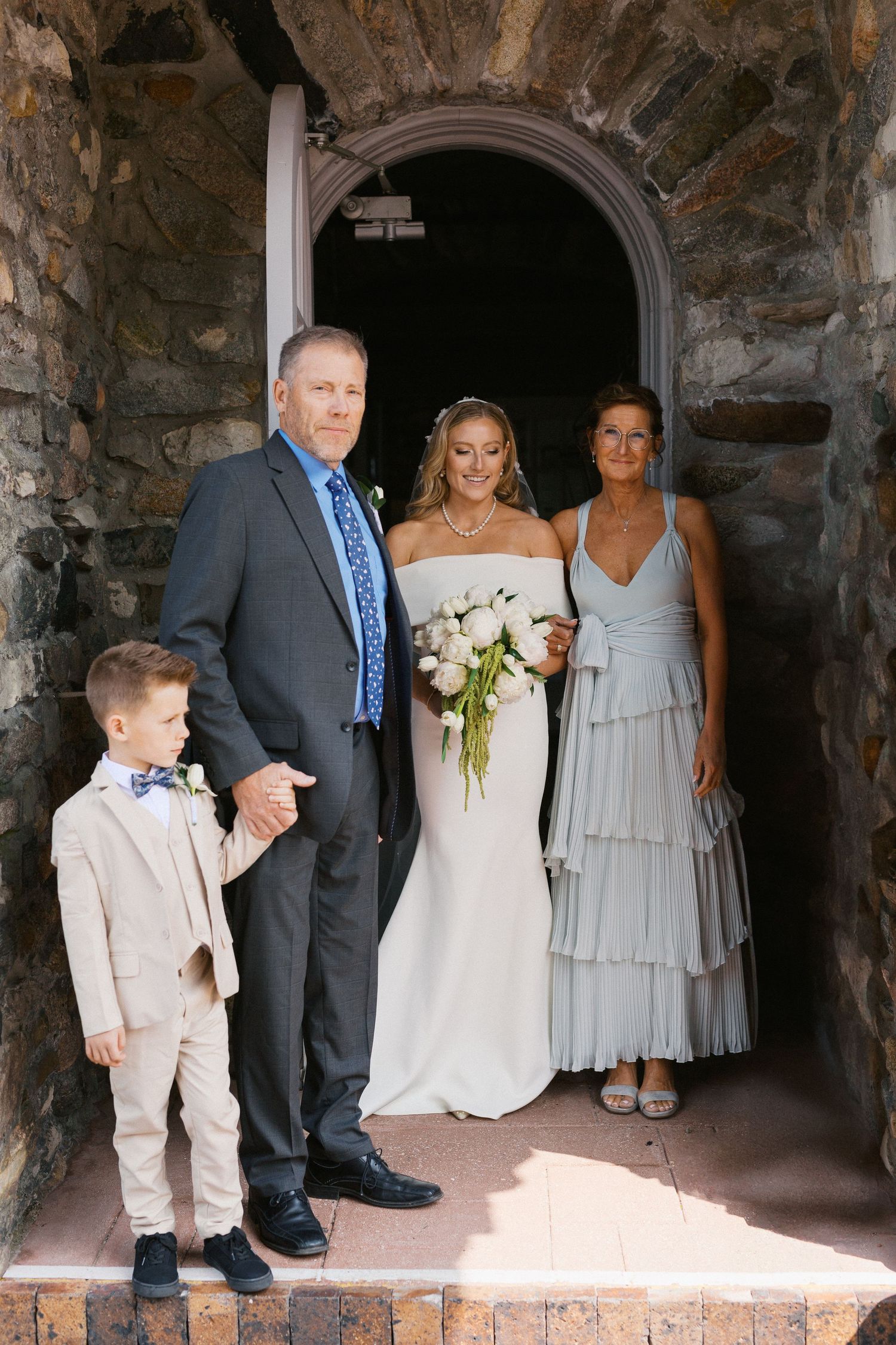 Wedding party gathered in a stone archway entrance for formal photographs.