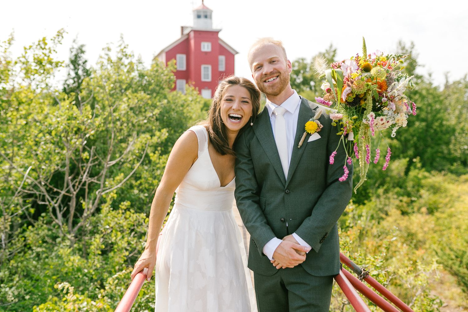Couple shares joyful moment in front of red lighthouse building with colorful flowers.