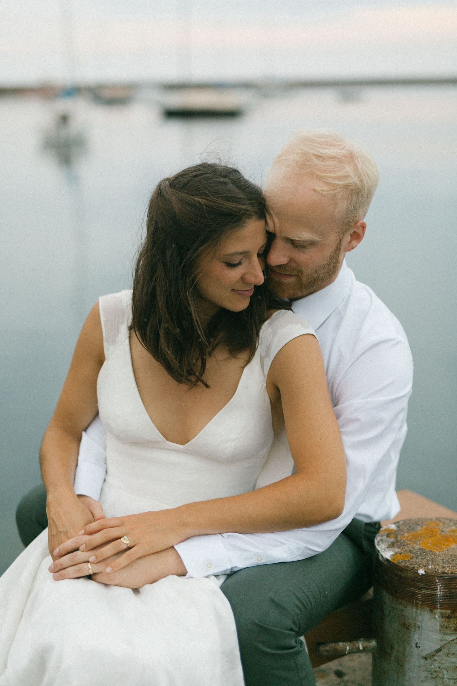 Intimate couple embracing on dock by calm water during sunset.