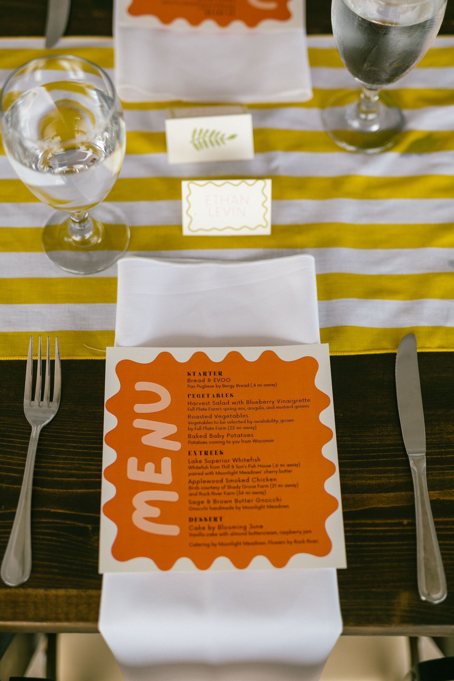 Wedding menu cards with orange accents on yellow striped tablecloths.