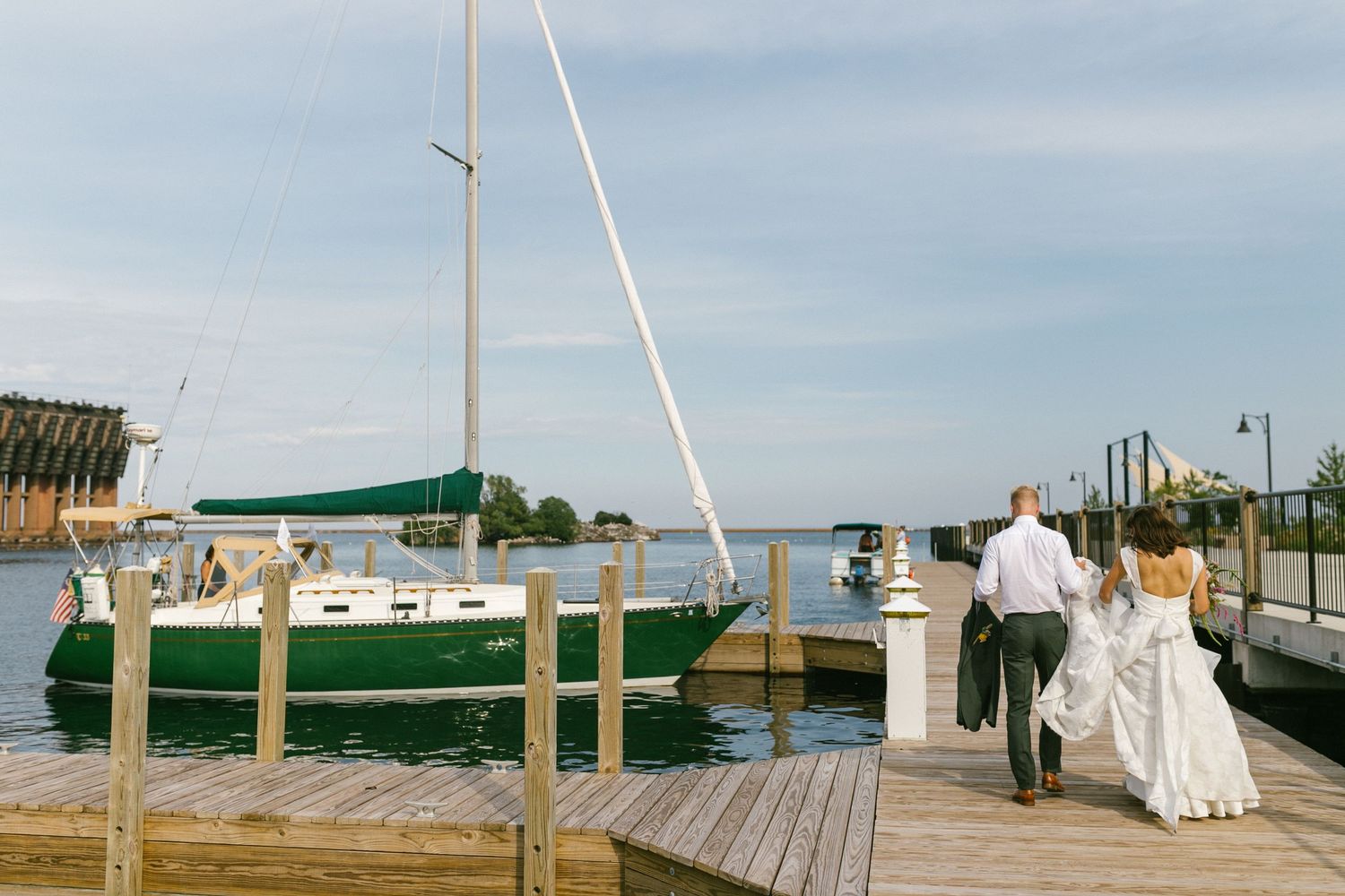 A wooden dock stretches out into calm waters with boats and masts visible in the distance.