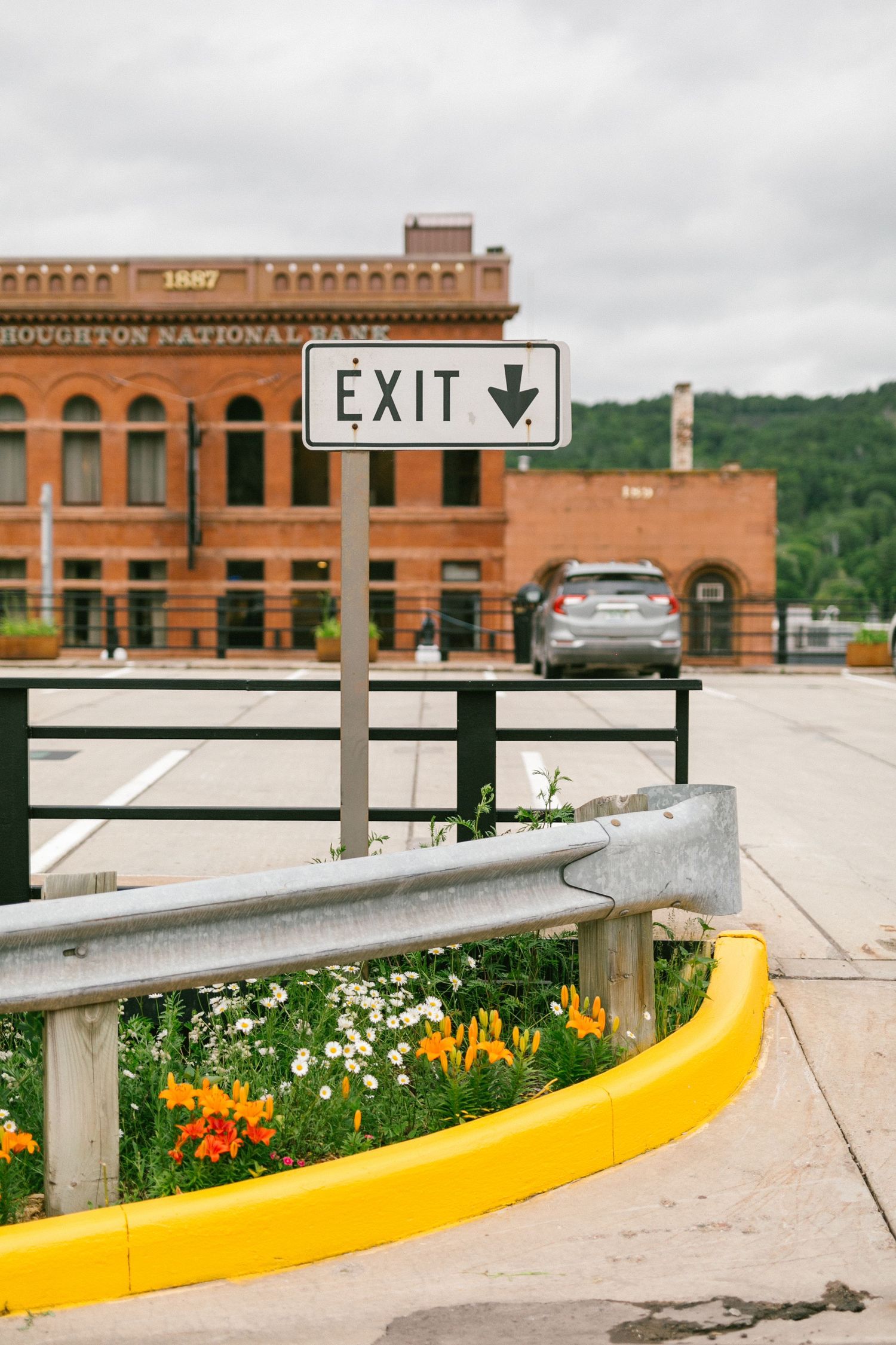 Exit sign and yellow curb near a historic brick building with colorful flowers in the garden bed.