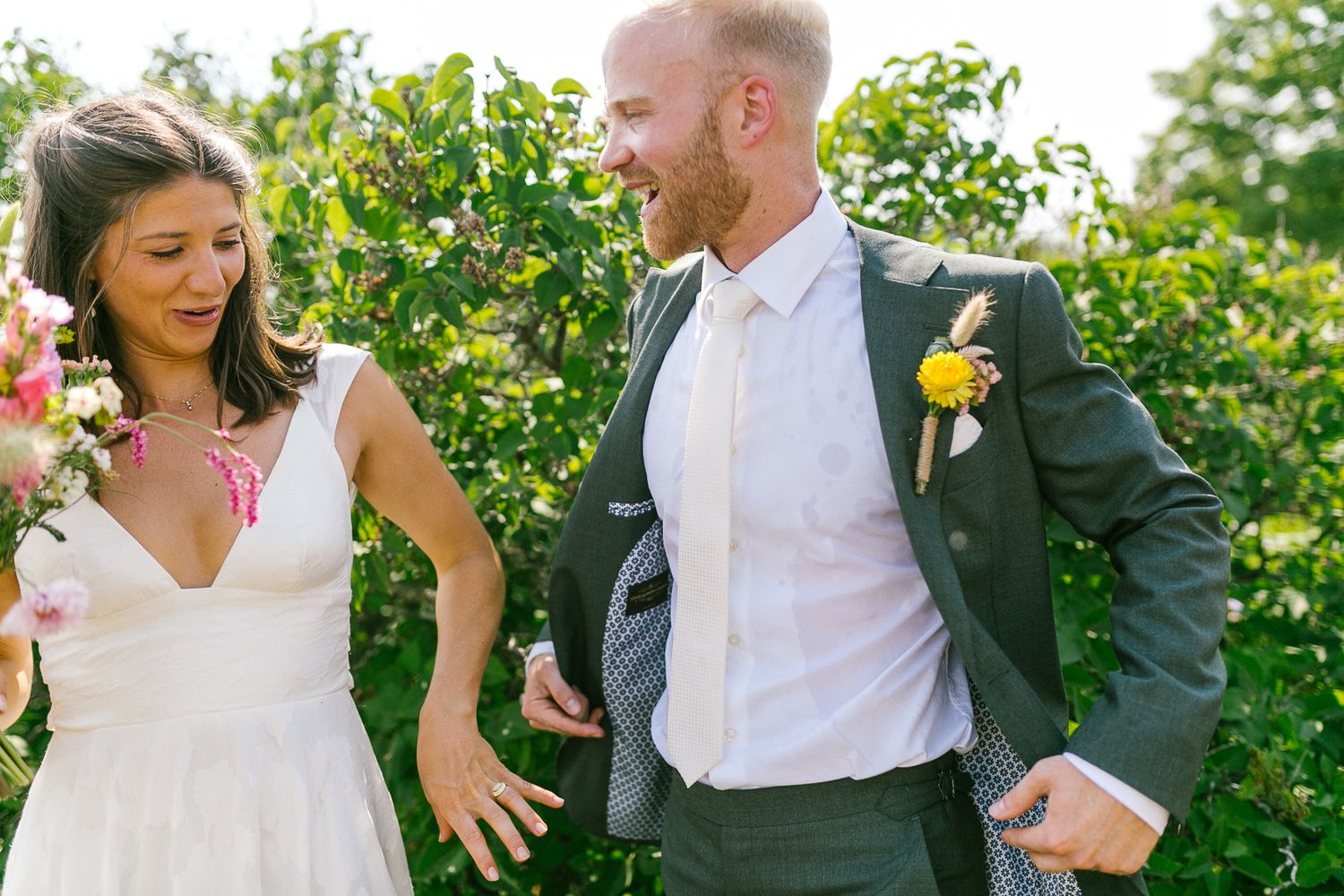 Wedding party members laughing and celebrating in a garden with vibrant greenery.