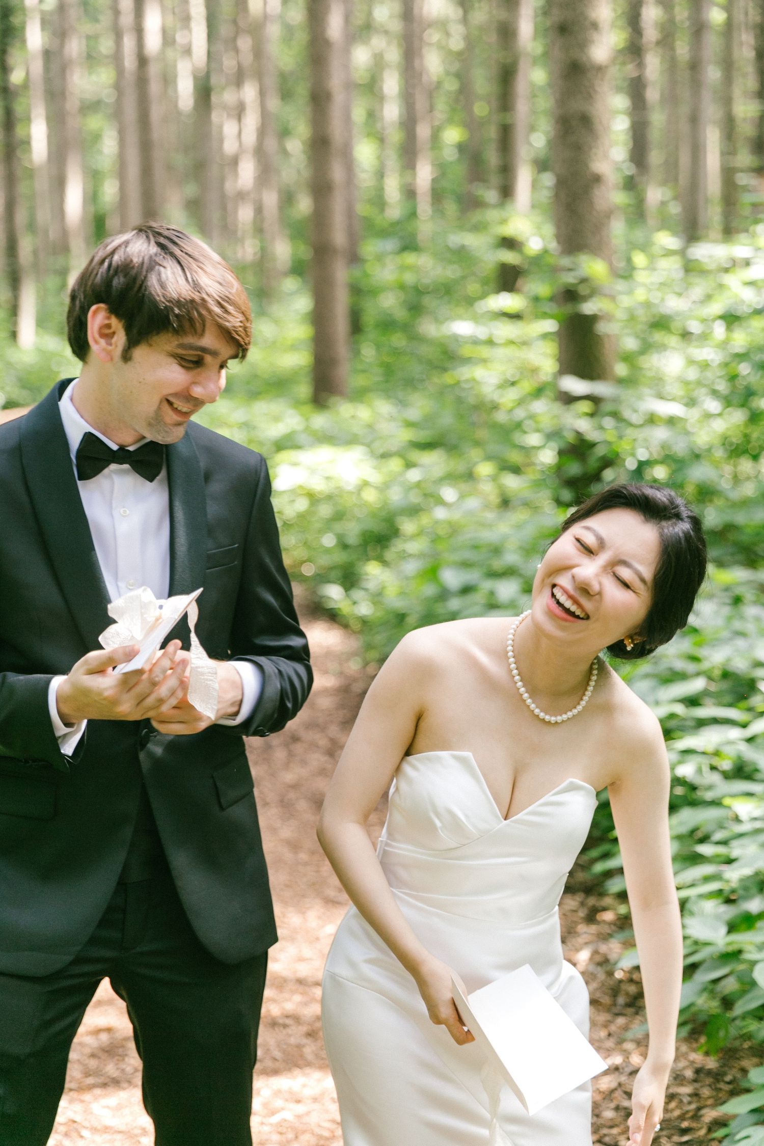 Laughing bride and groom sharing vows letters in a lush green forest.