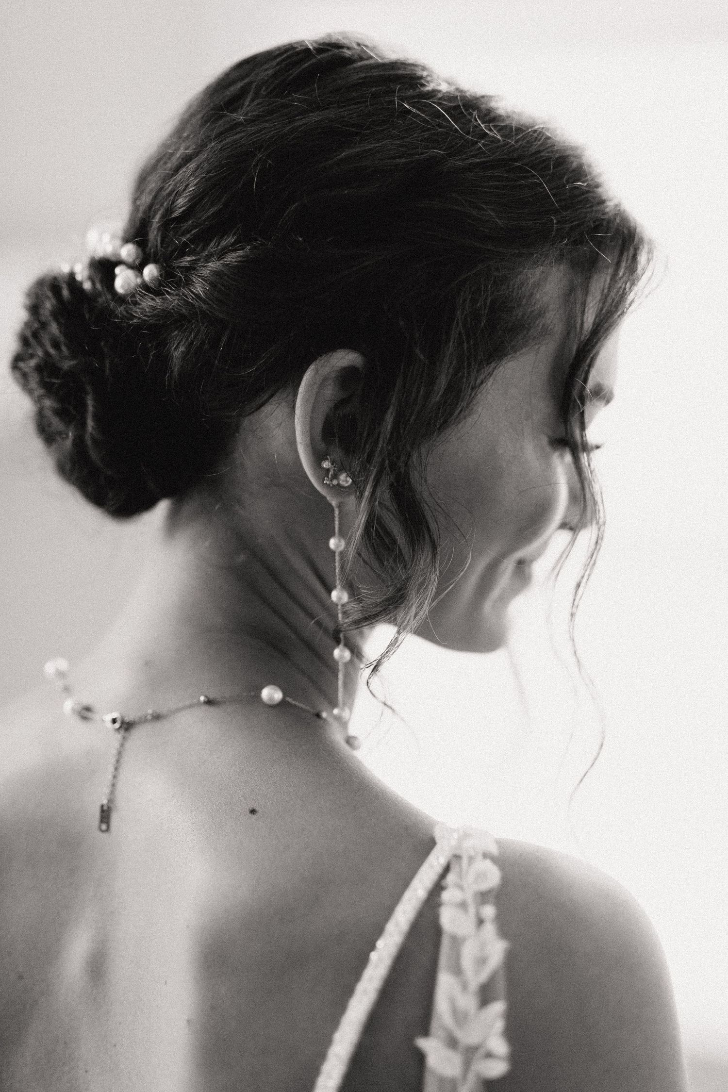 Black and white elegant bridal portrait showing delicate pearl jewelry and an updo hairstyle with soft wisps in profile view.