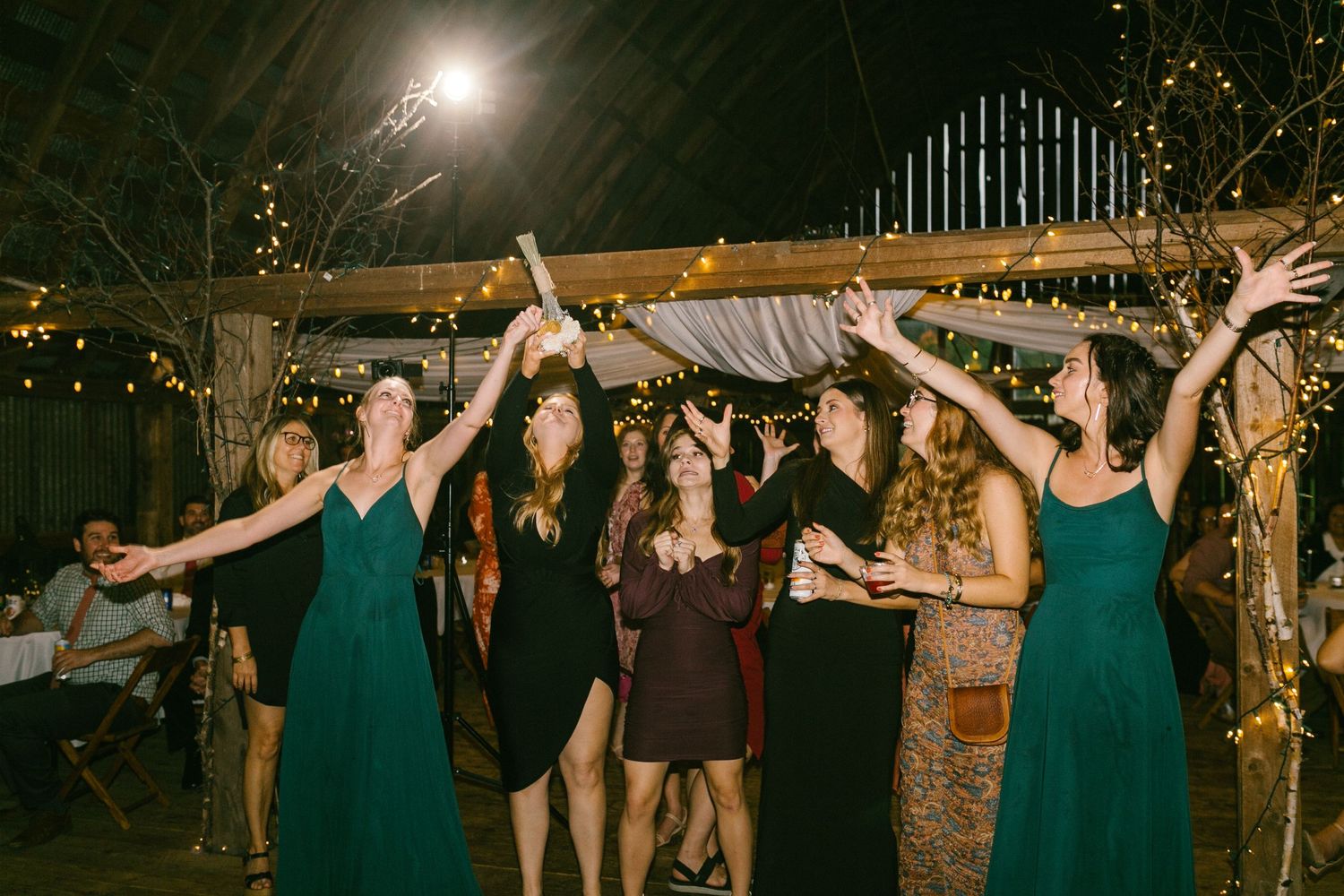Guests dance and catch a bouquet under twinkling lights at a lively wedding reception.
