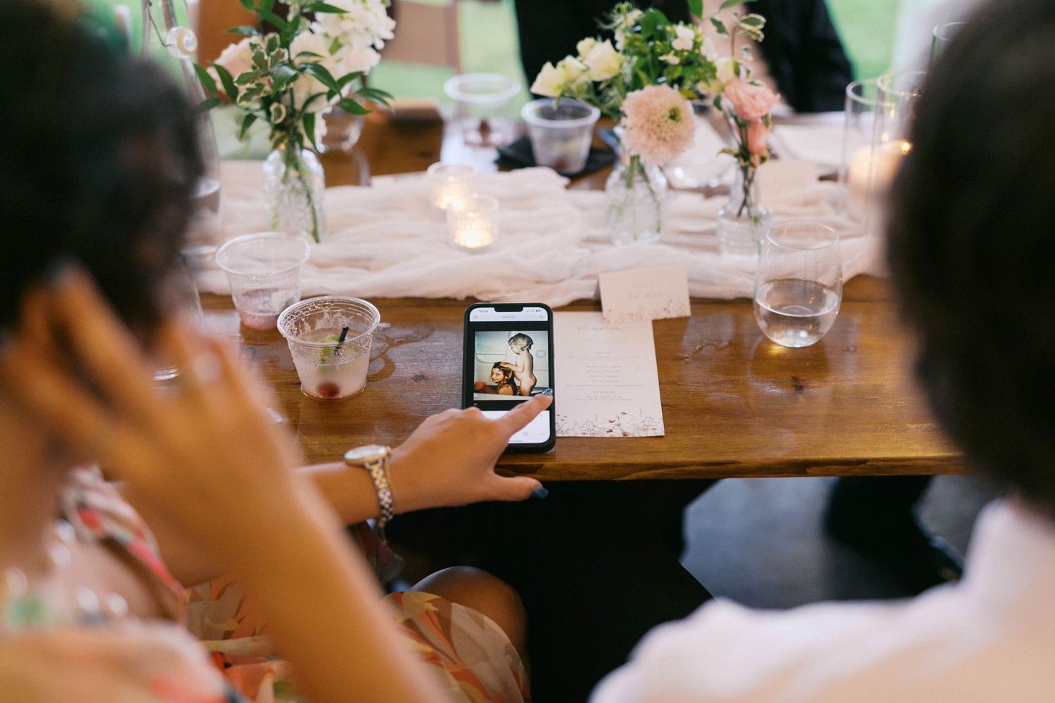 A group of people gathered around a rustic wooden dining table with glowing string lights overhead.