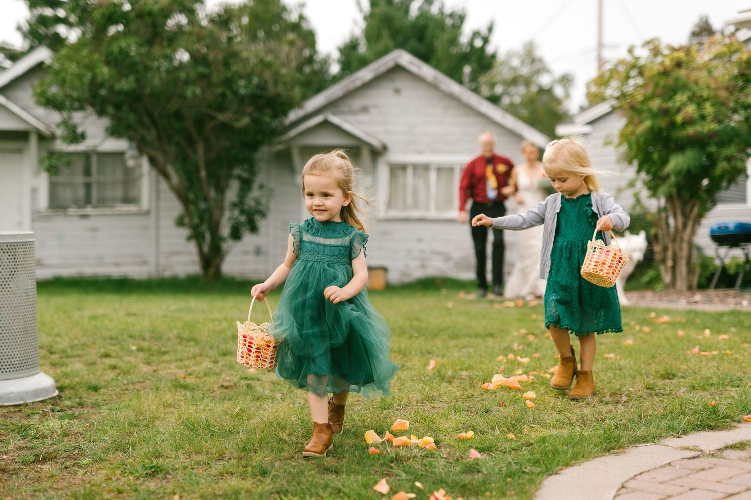 Two children wearing matching teal dresses play with autumn leaves scattered on a front lawn.