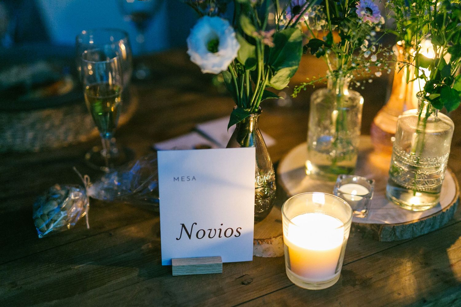 Table setting with Novios place card, candlelight, and delicate floral centerpieces in glass vases.
