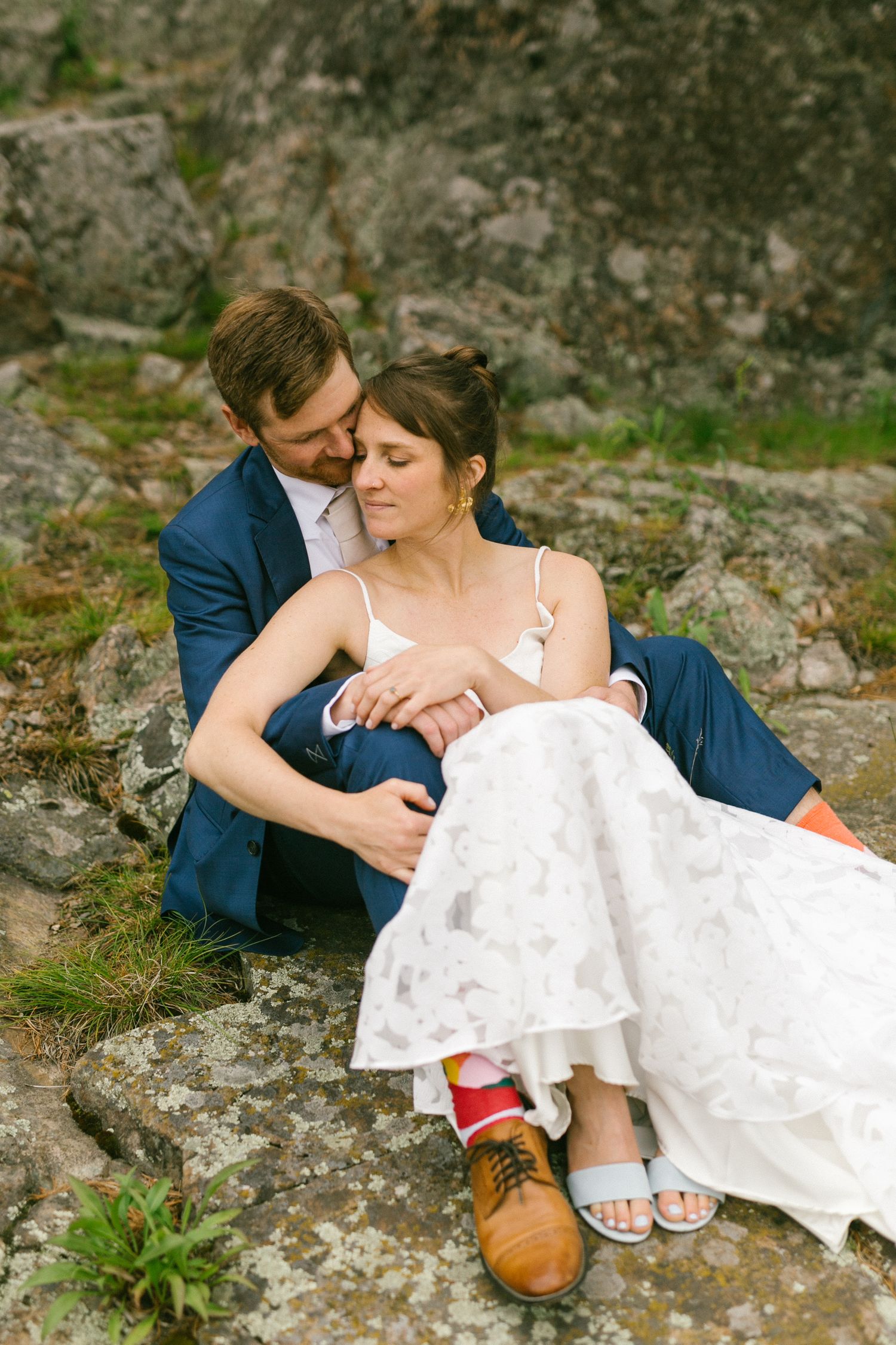 A couple in wedding attire sits intimately on mossy rocks during a romantic outdoor photo session.