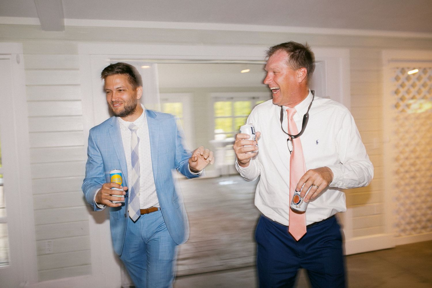 Guests in light blue suits enjoying drinks and conversation at indoor reception.